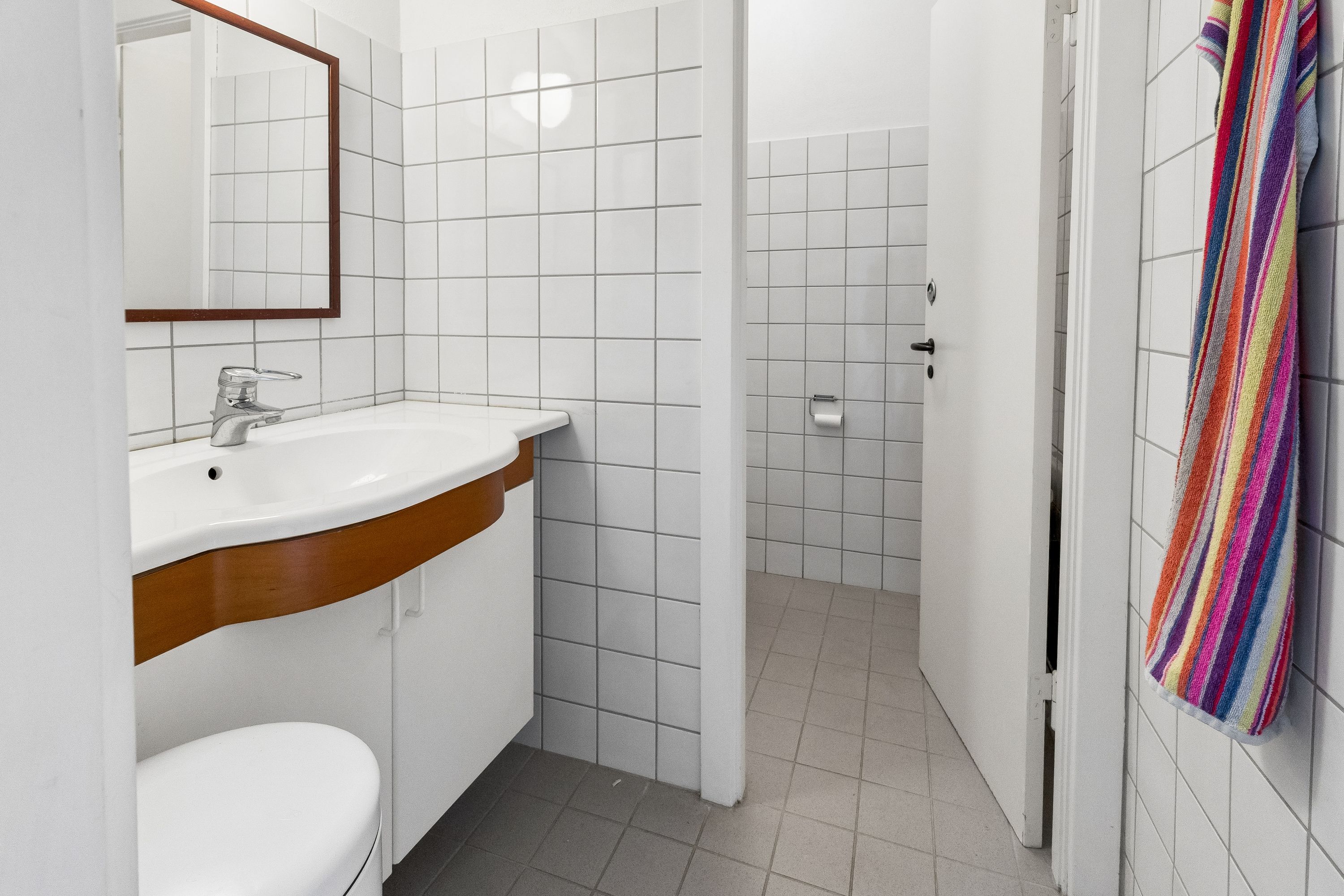 Toilet med hvidt badeværelse, lysegrå gulvfliser, ren toiletforstærkning, hvidt badeværelsesskab og håndklæde på hængehylde med stribet design