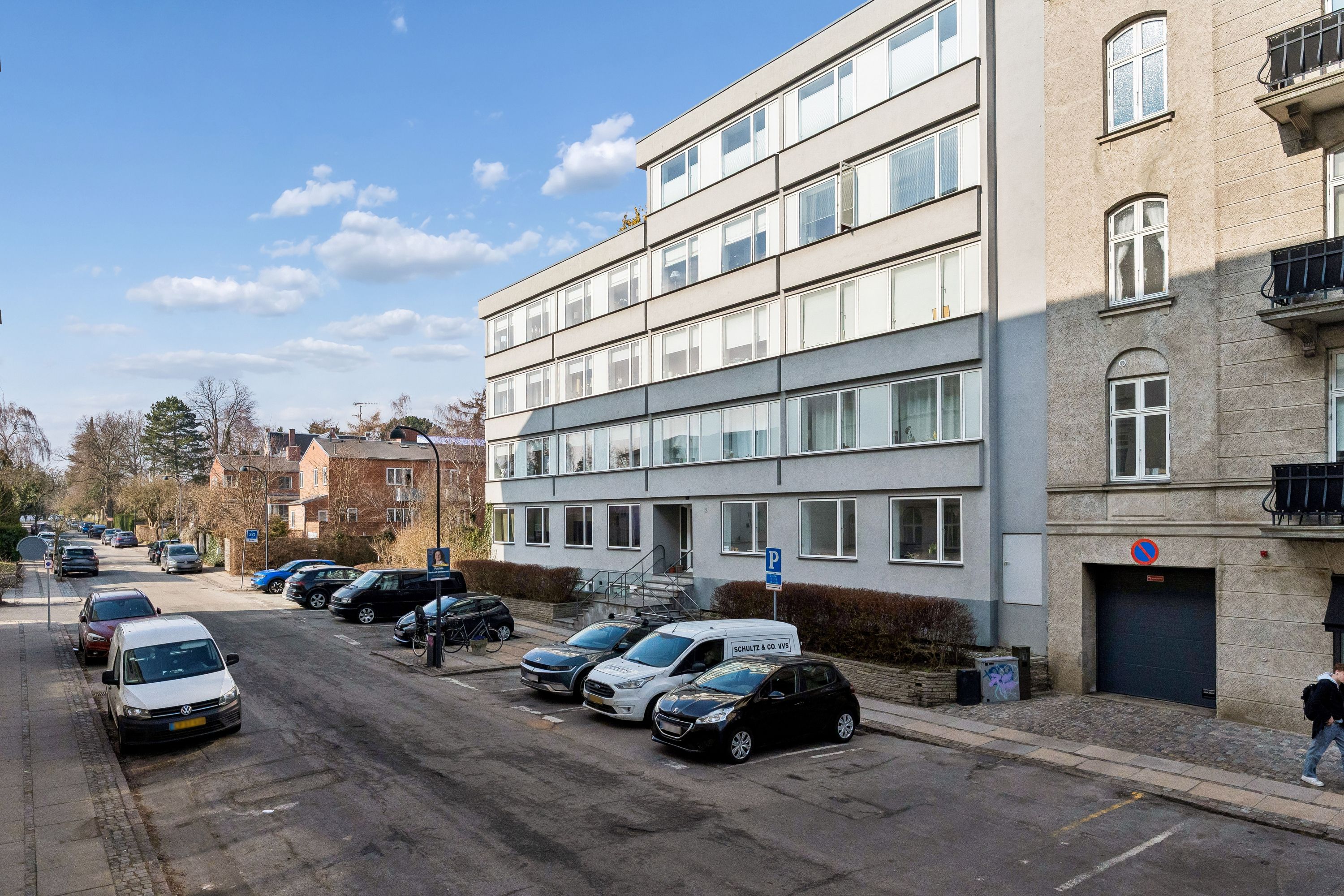 Kontor til leje i Aurehøjvej 2, Hellerup. Flere biler parkeret på gaden og gågade med personer. Bygning med parkeringspladser og biler parkeret.