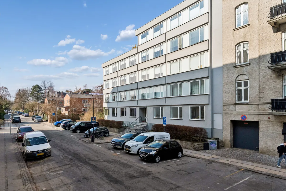 Kontor til leje i Aurehøjvej 2, Hellerup. Flere biler parkeret på gaden og gågade med personer. Bygning med parkeringspladser og biler parkeret.