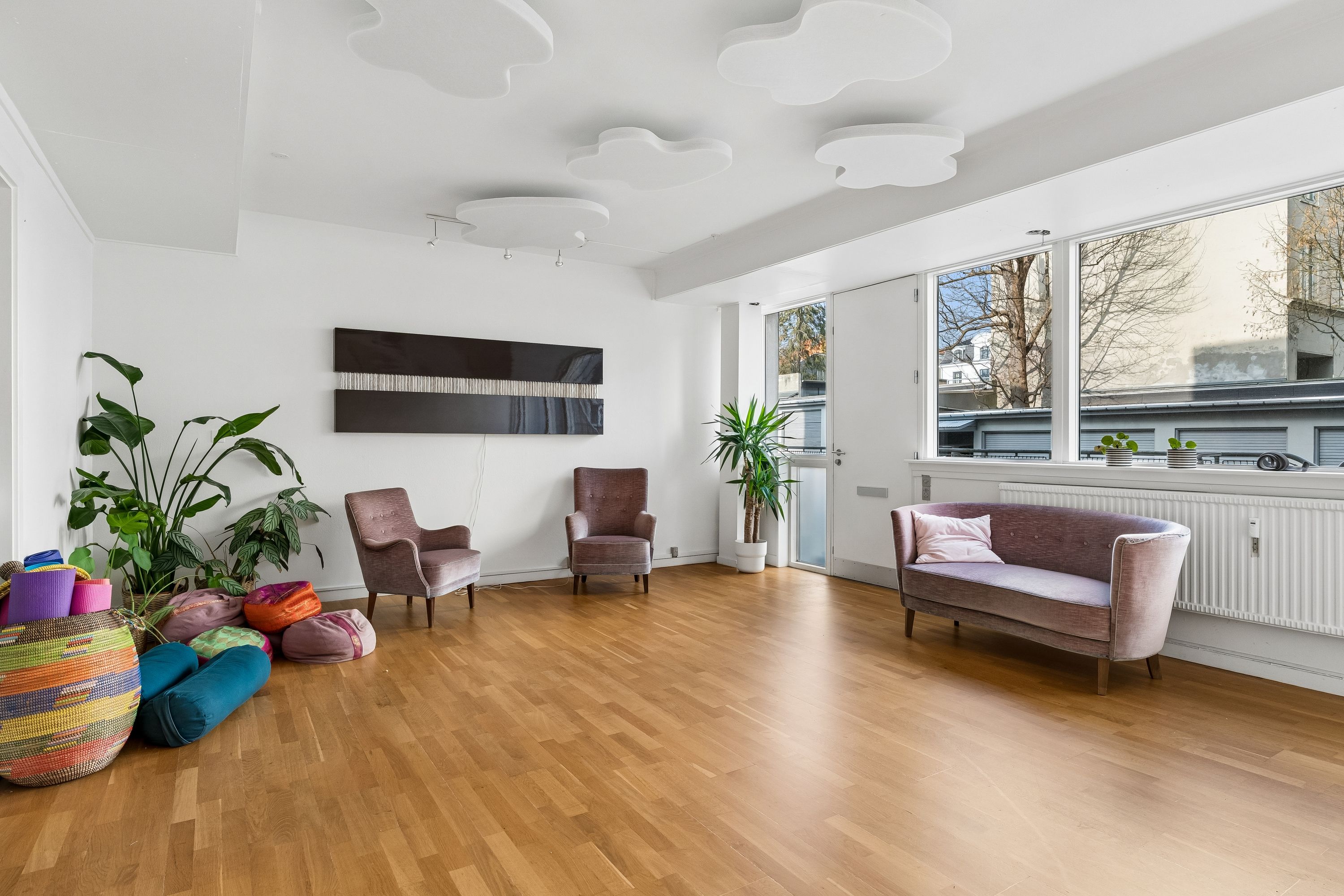 Kontor med lys og rummelige værelser, hvide vægge, trægulv, komfortable sæder og plante. En stor plante i krukken og flere lyse skulpturer på loftet