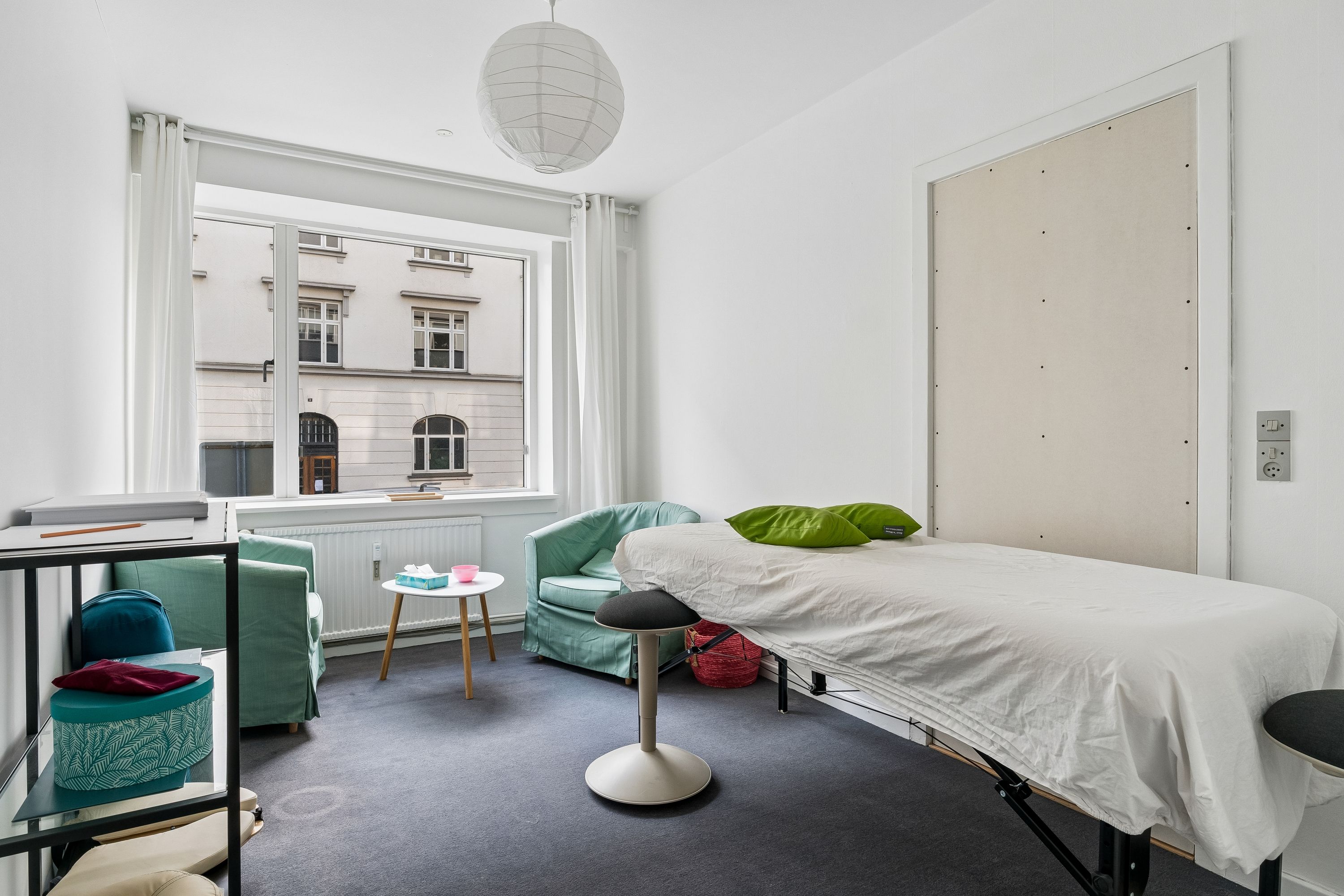 Kontorrum med massivt hvidt og lysegråt, trægulv og lysegrå vægge. Sengetablet med hvidt linc og grønne pude. Lampen er hvidt og rundt.