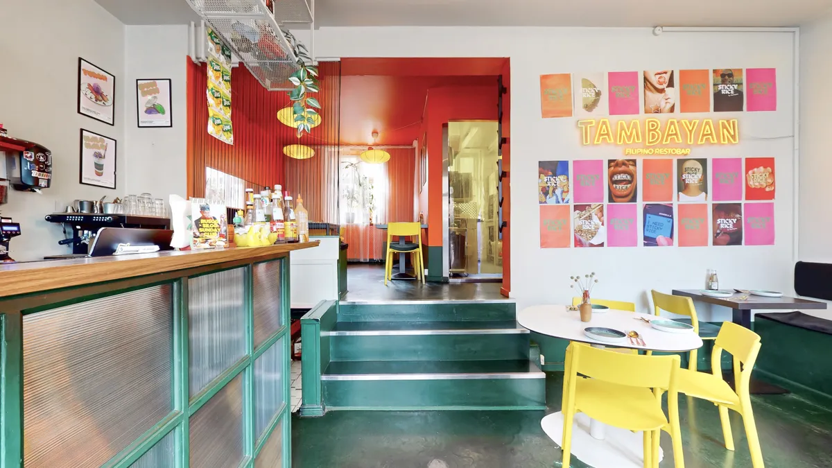 En lys café med lysegul og røde vægge og gulv, med borde, stole, og en åben dør til bagværksrummet