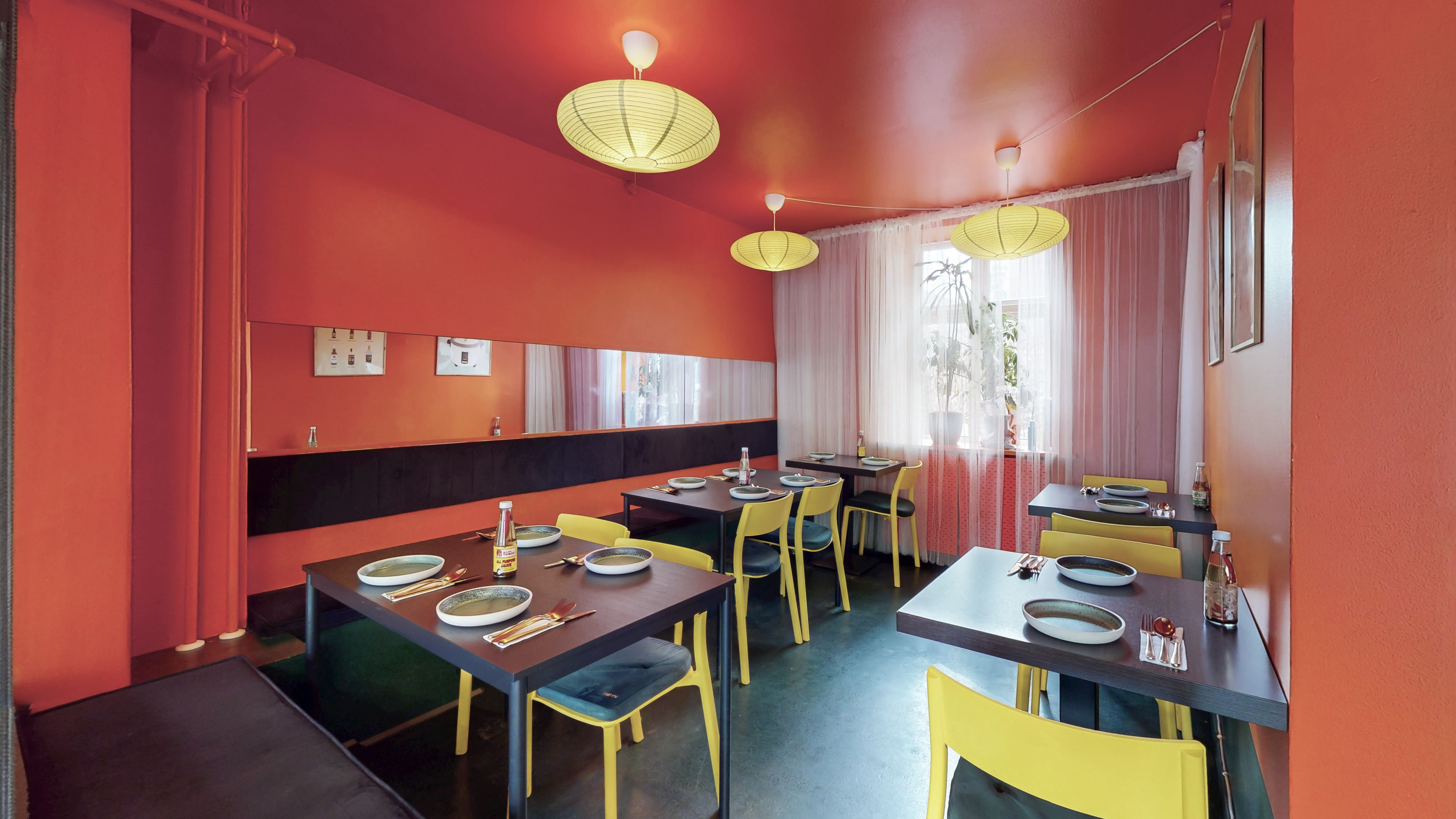 Inde i et moderne restaurantområde med lysegult og rødt interiør, hvor der er spisesteder med borde og stole samt lyse lysekroner