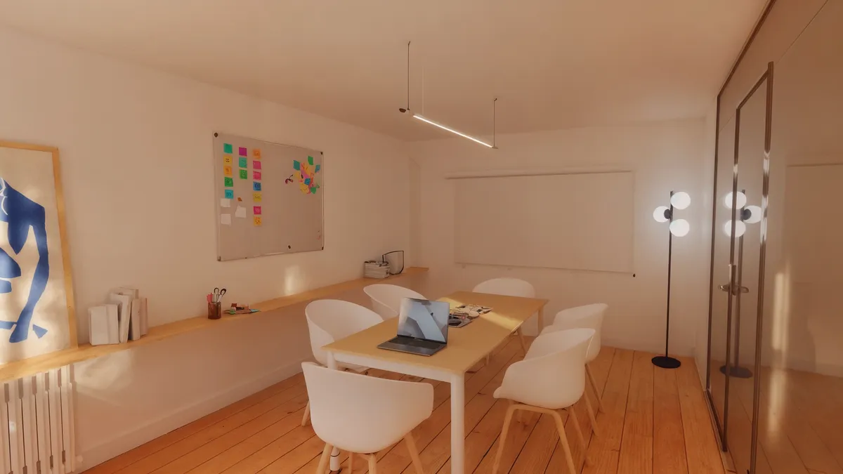 Et kontorlokale med lyse vægge og trægulv. Væggen er dækket af en magnetbord med post-it noter. Et skrivebord med computer og briller og en lampe.