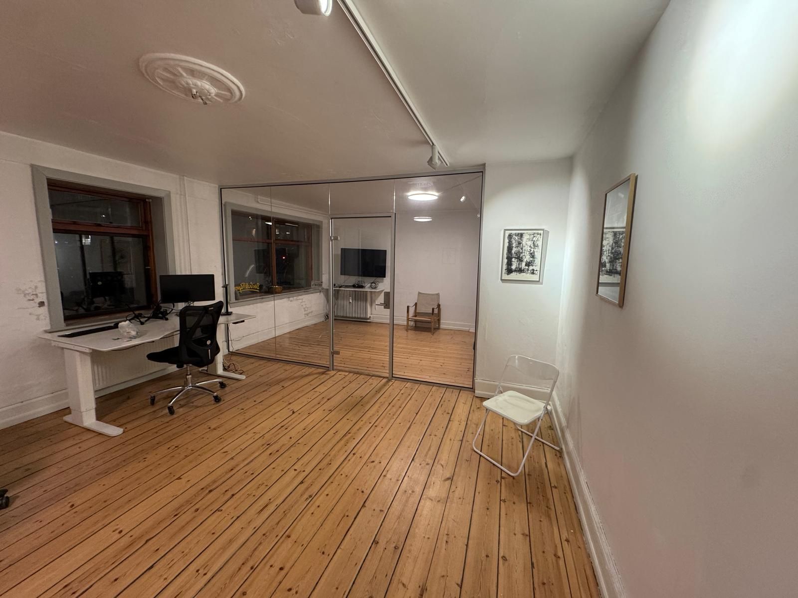 Kontor med højt gulv, to skriveborde og to stole samt en stor spejldør og to kunstværker på væggen