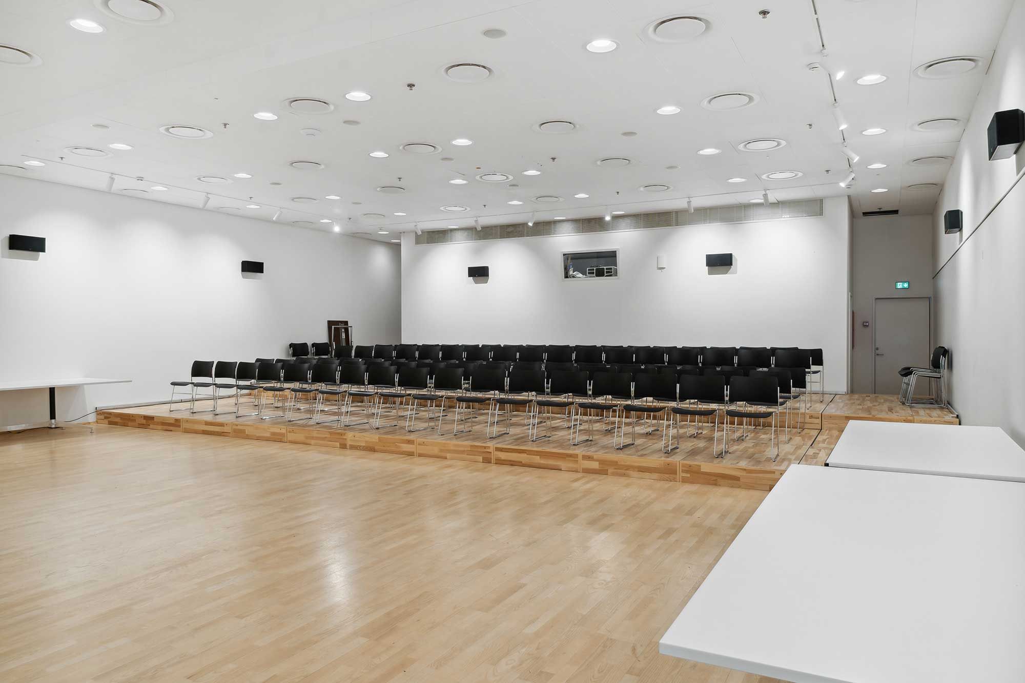 En stor auditorium med lyse loftslamper, hvide vægge og møbler og lyse trægulve