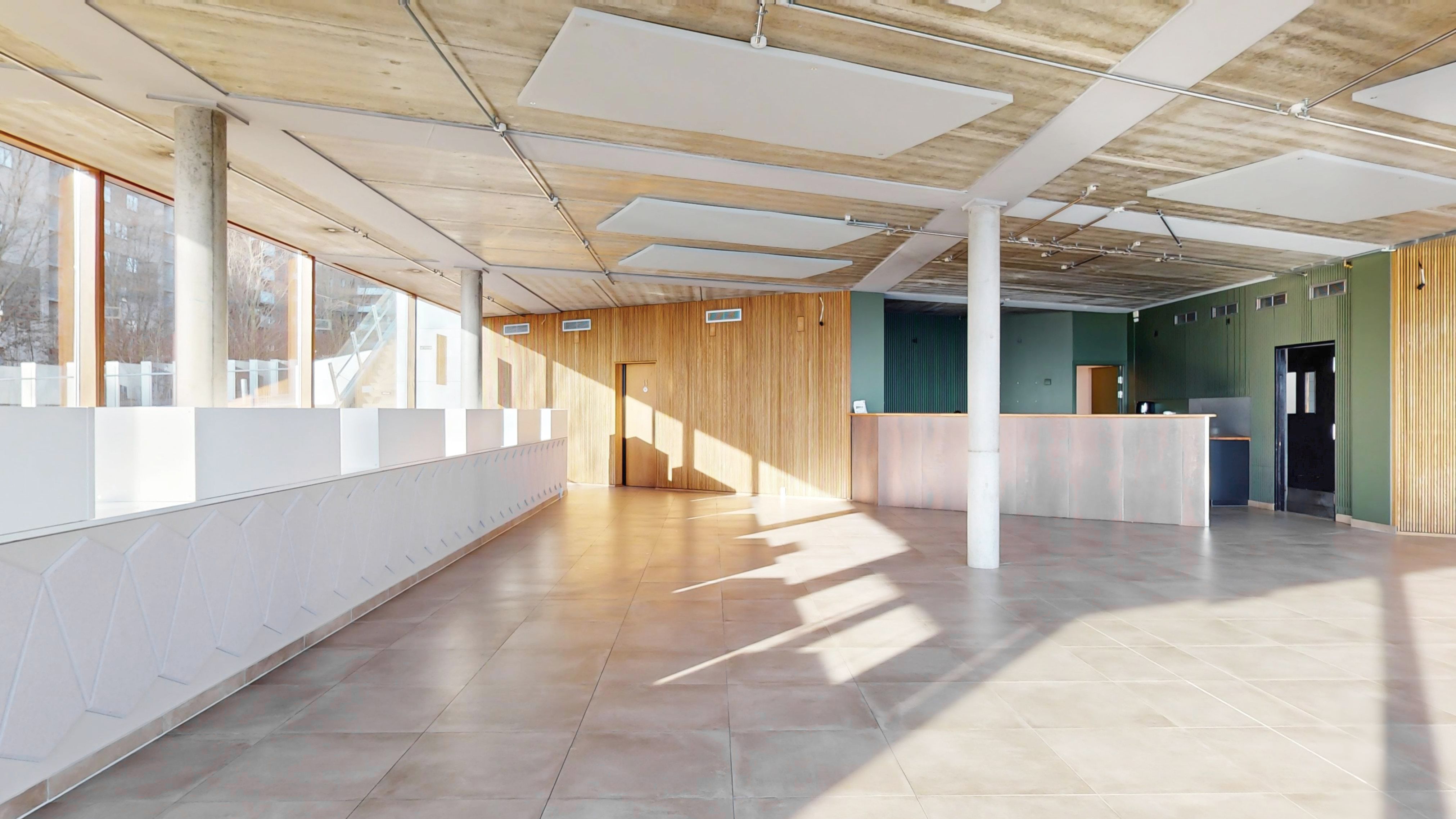 Indgangsparti med højt loft, lyse og store vinduer og lysegul gulvbelægning i Ørestad. Store lysepartier og en flot, hvid og træslægt facade.