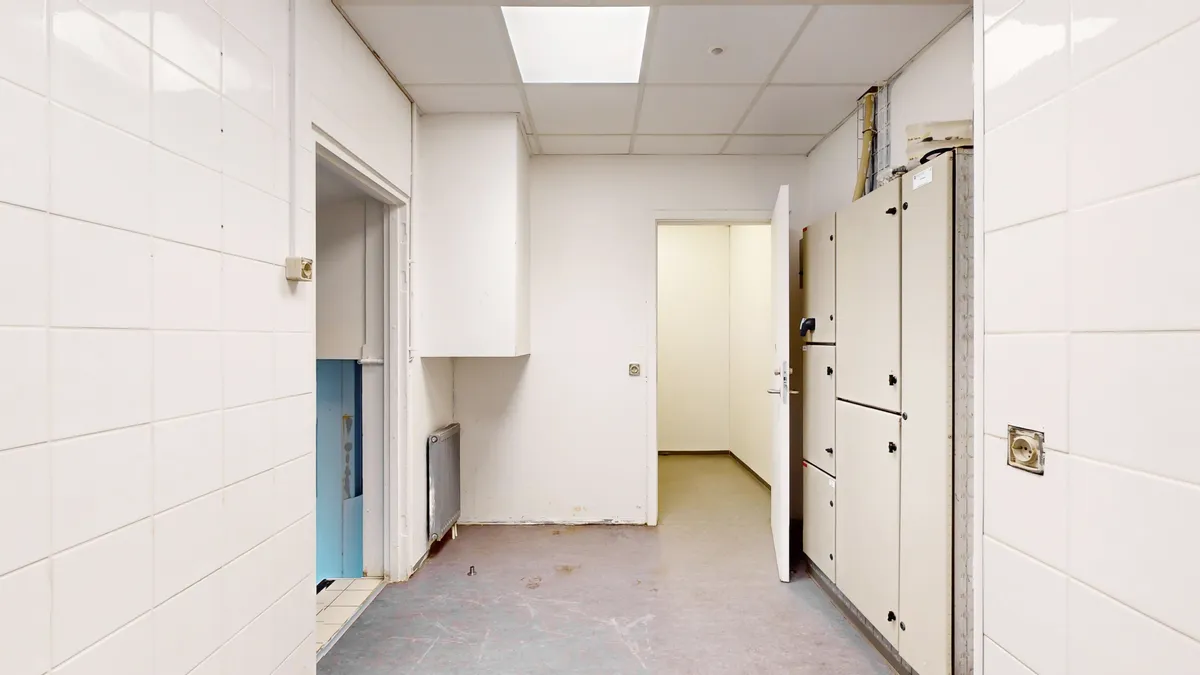 En stor rummelig og lys hall med hvide vægge og loft, åbne døre og kabinetter samt radiatorer og elektriske stik.