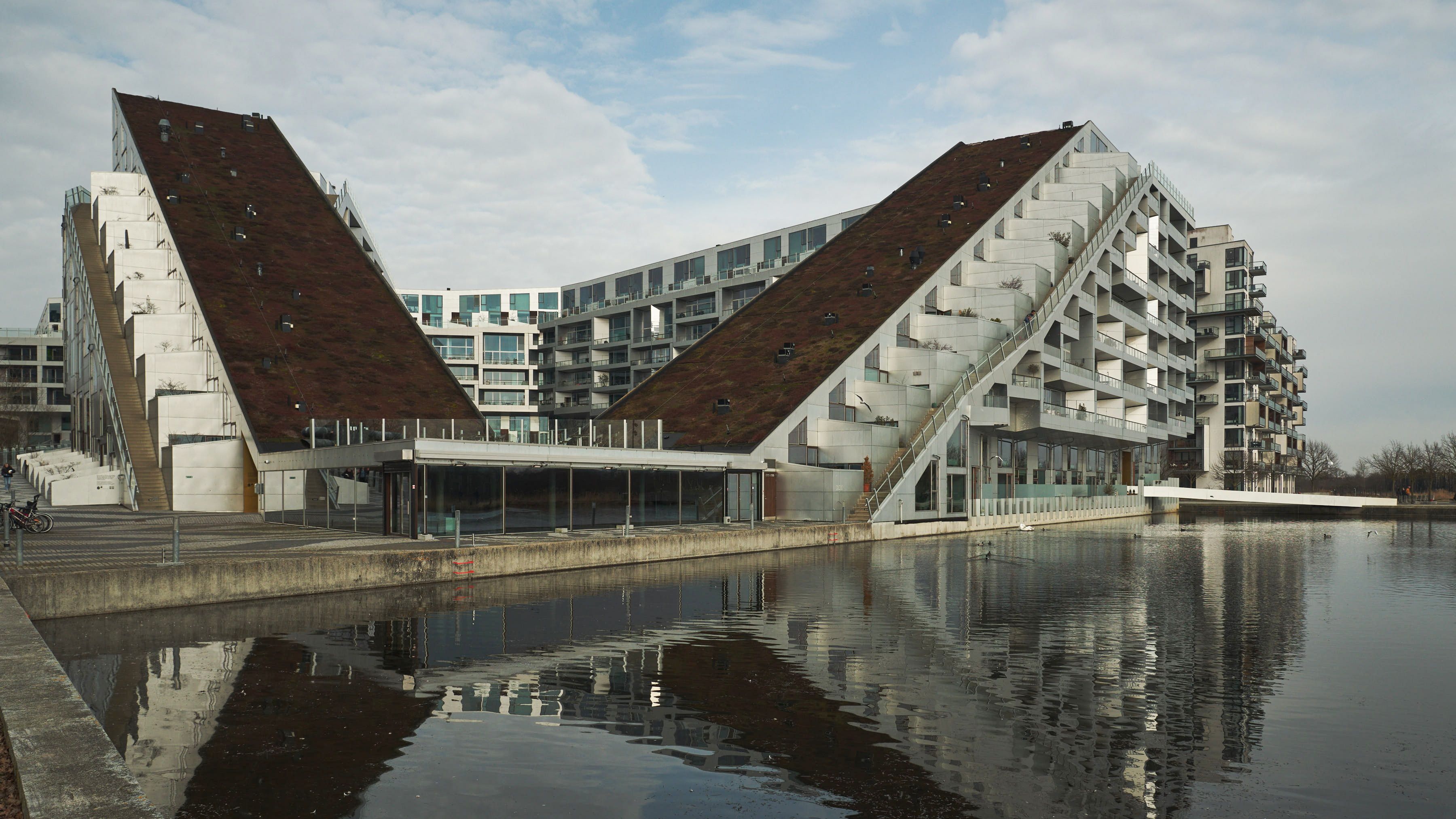 Moderne bygning med grønt tag og trapper ud til vandet i Ørestad, København med glas facader og terrasser