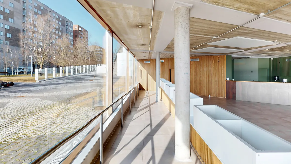 Moderne lejemål med hvid marmorgulv og stålsøjler, høje vinduer og lyse interiør. Inde i lokalet er der hvide bænke og træbeklædte vægge.