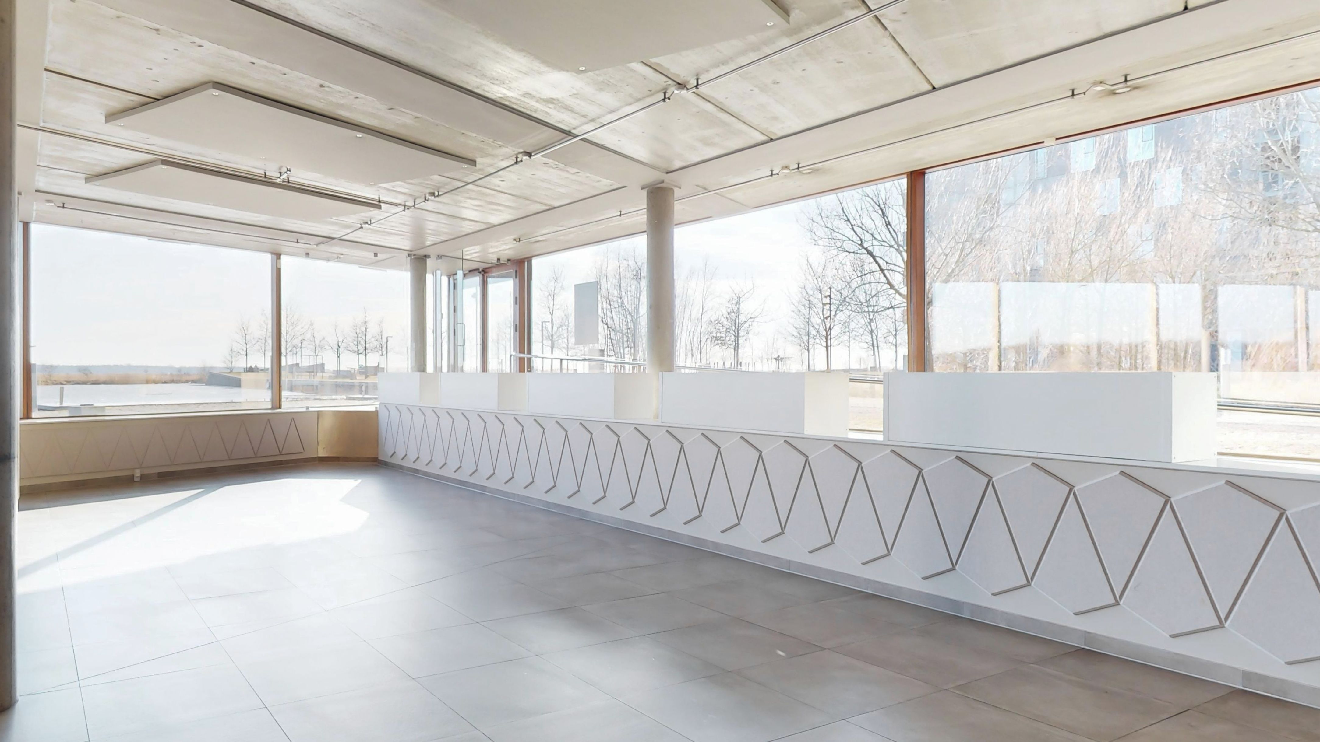 Store, lyse vinduer med udsigt til skov og vand i baggrunden. Moderne, hvidt gulv og vægge. Minimalistisk og stilren indretning med rektangulært design