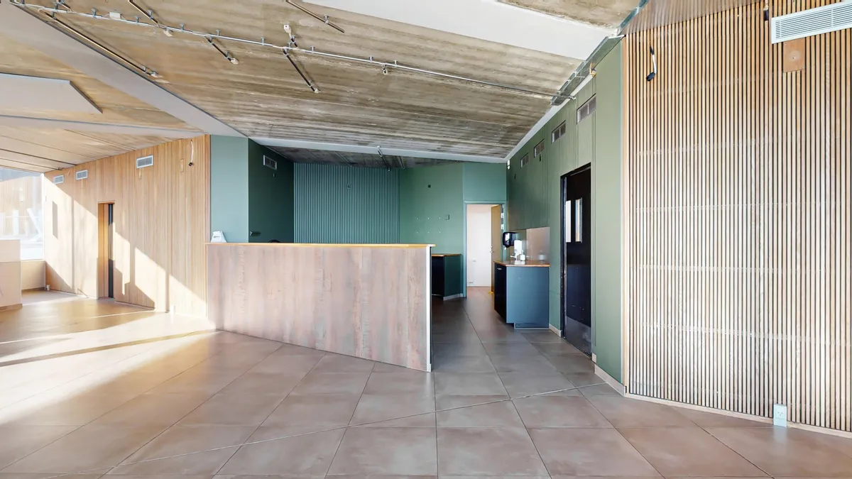 Hvidt loft med lyse nuancer og store vinduer. Sort og grøn farvekombination på vægge. Trægulve og en massiv træbar.