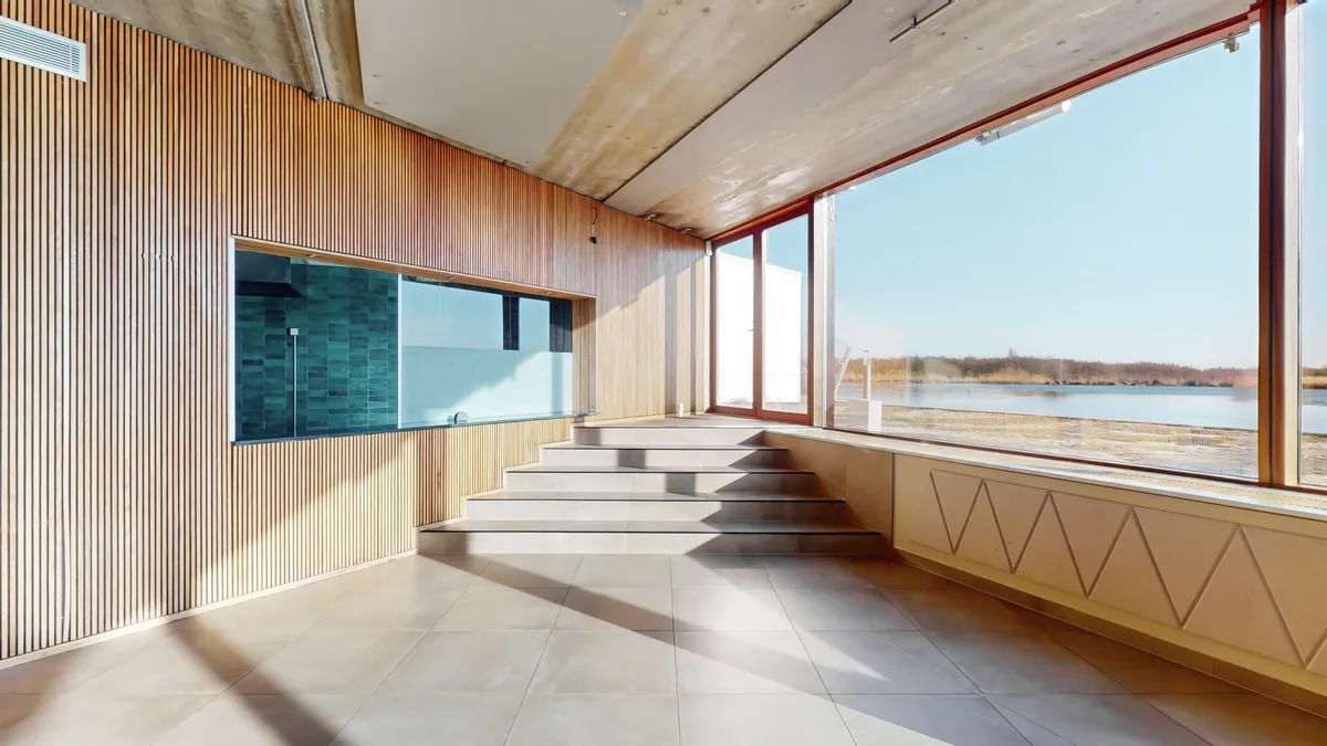 Lys og rummeligt rum med gult gulv og mønstret træbeklædning, trapper og vinduer med udsigt over vandet og landskabet