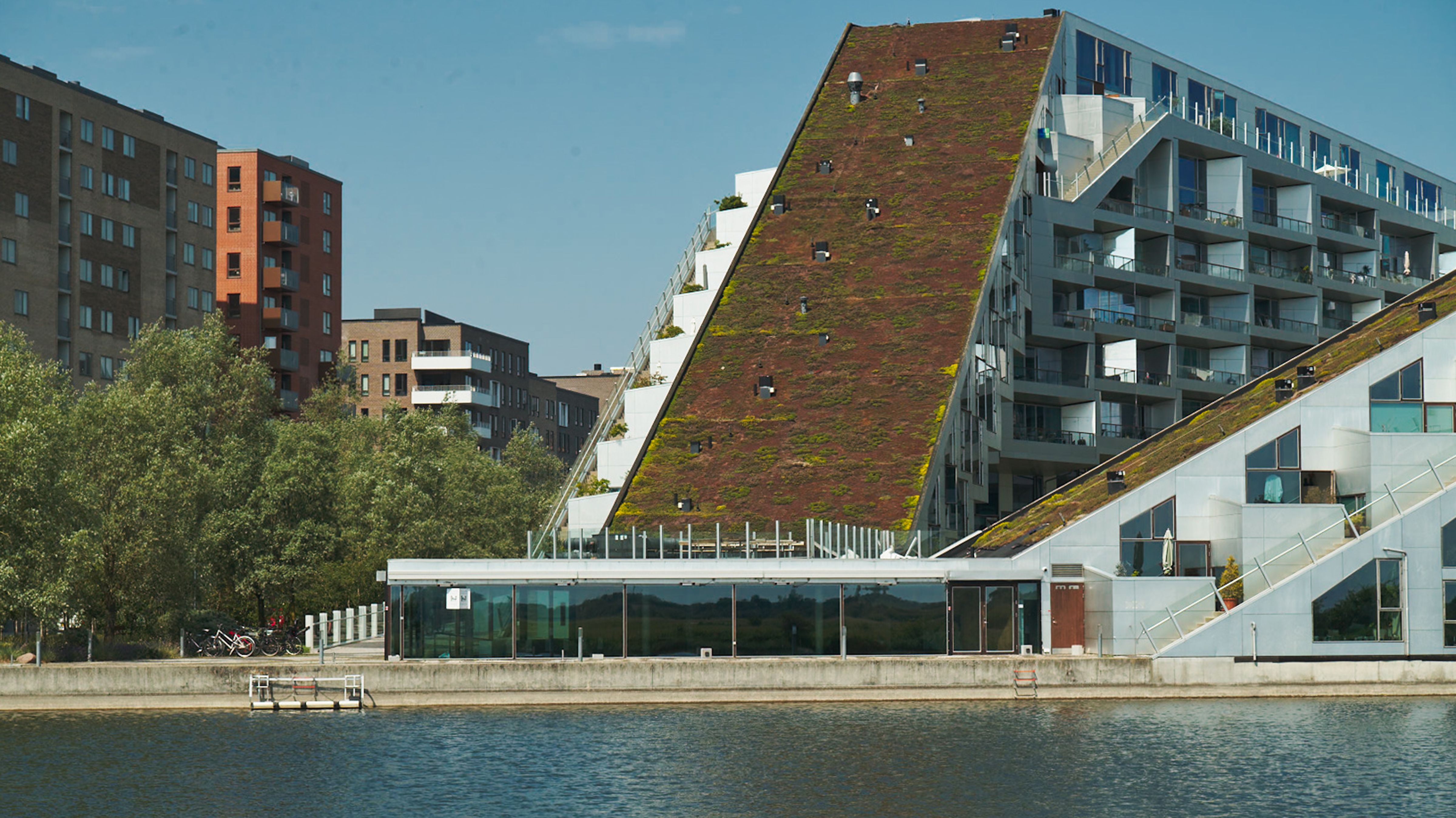 Moderne bygninger med grønne tag i Ørestad, København S. Træer og en sø i baggrunden. Moderne arkitektur med grønne tag.