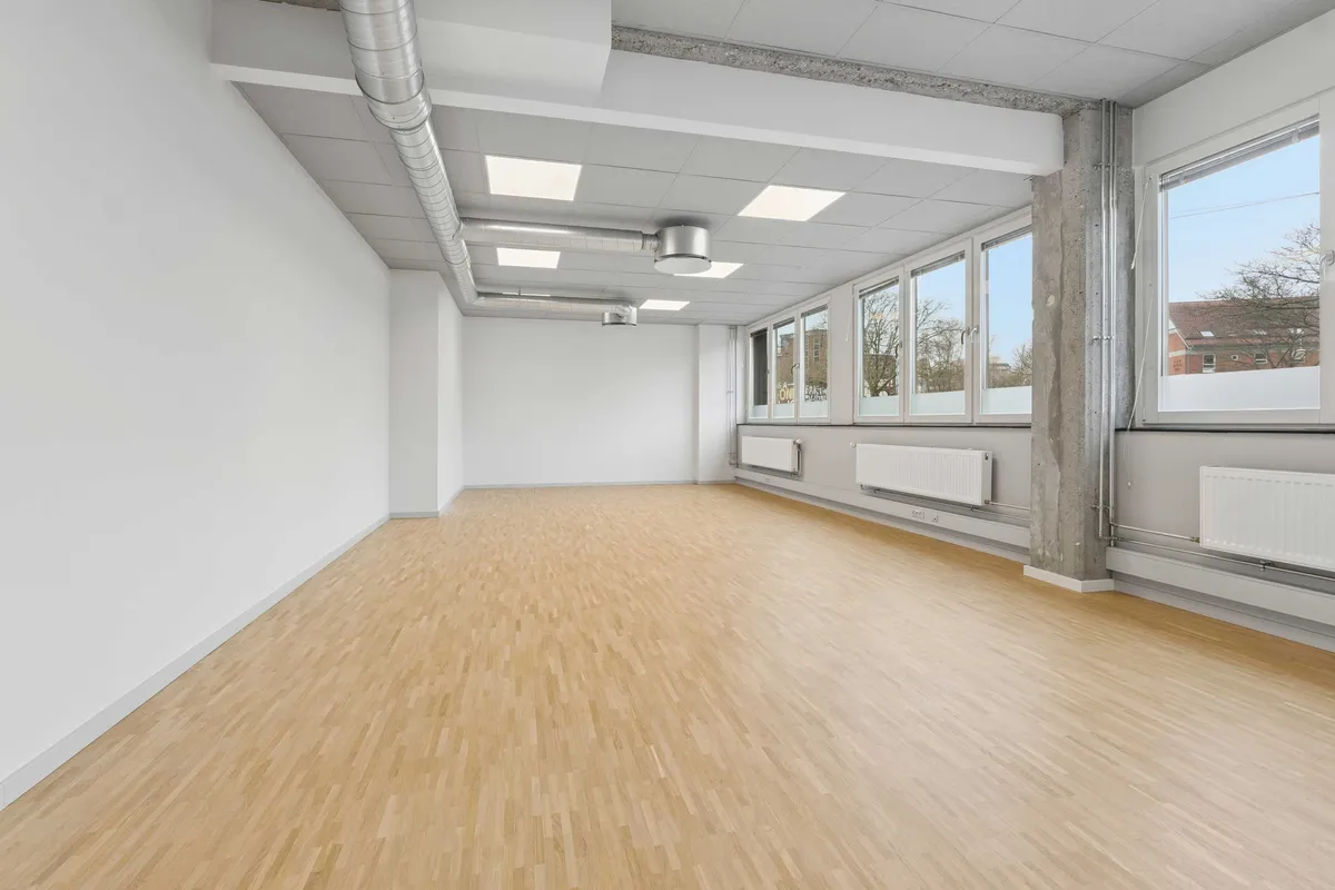 Rønnegade 4, København Ø. Rummelig, møbleret kontor med lyse gulve og store vinduer. Væggene er hvide, og der er højt til loftet med lysepunkter og luftkanaler