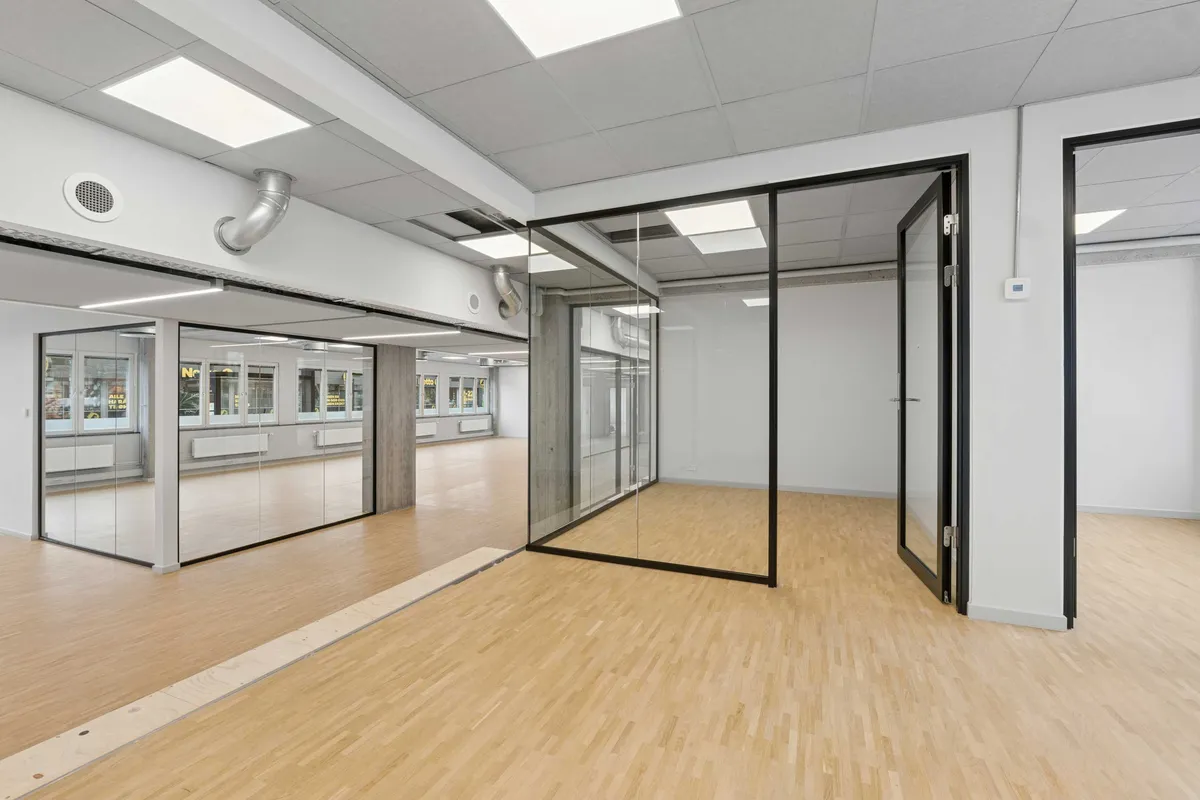 Hvidt lokale med højloft og glasvægge. Efterlad en kommentar til lokalet. Luftkanaler og ventilationshætte er installeret i loftet. Væggene og gulvet er lavet af træ