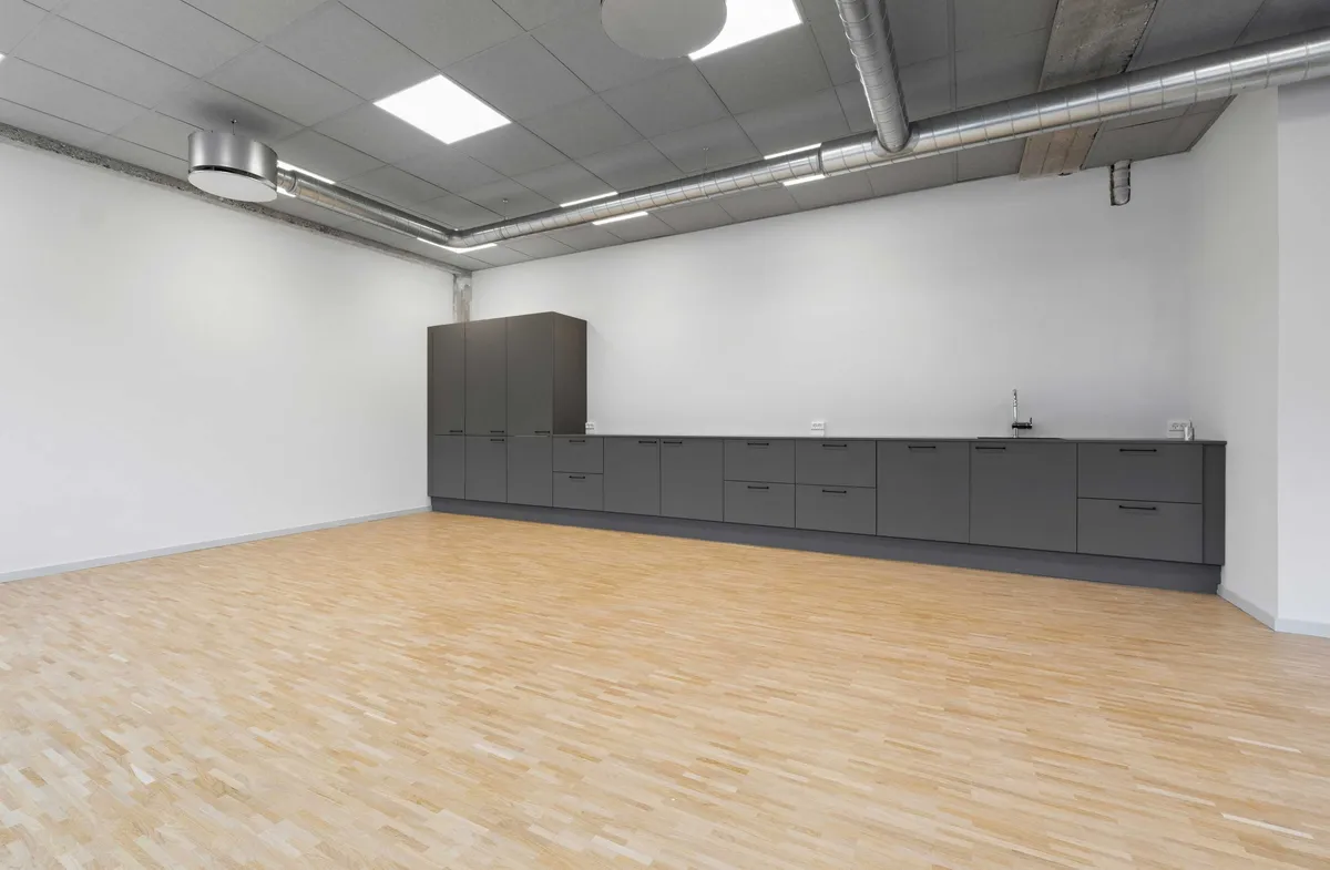 Et stort, tomt kontor med moderne design, hvidvaskede vægge og lyse loftspaneler. Store trægulve og kompakte møbler. Et lysfiksatur er hængt i loftet.