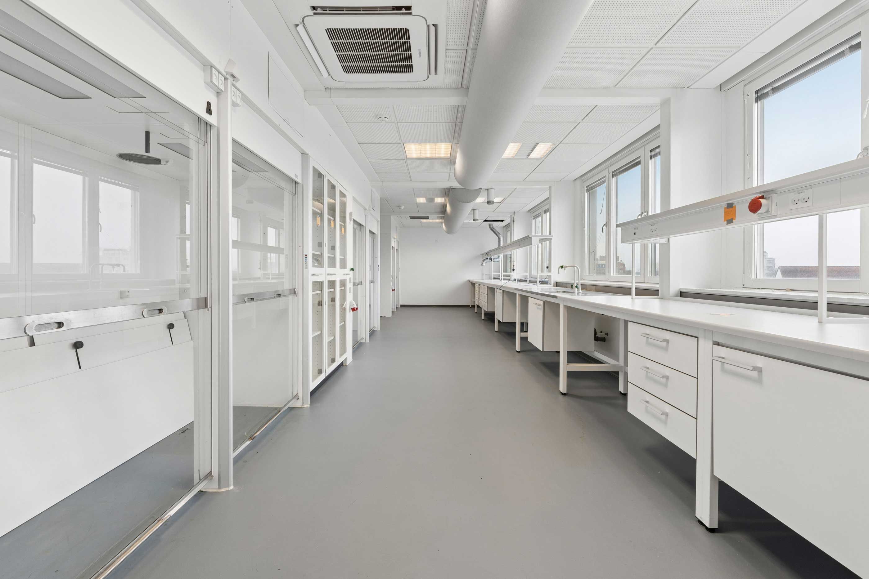 Moderne laboratorium med hvide vægge, glasdøre og lysevinduer, smukke kontorer med højt loft og søjler og gulvbelægning med stærkt udtryk