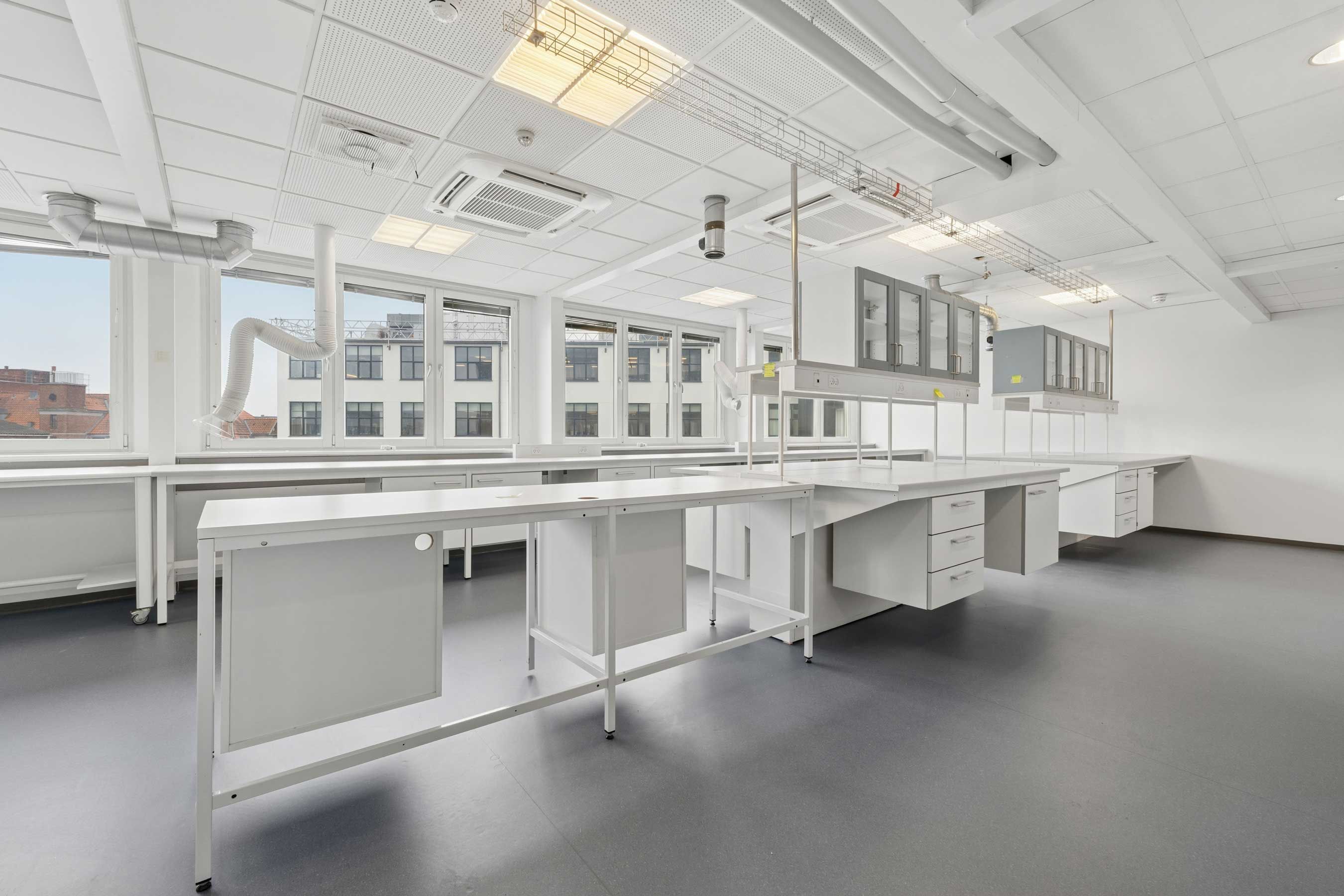 Moderne og lyst laboratorium med lyse, hvide vægge og store vinduer, hvor flere lysekroner er monteret på loftet.