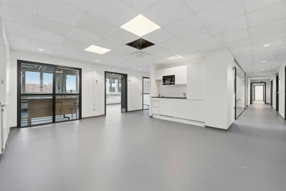Lyst laboratorium med moderne møbler, glasdøre, lyse lofter og hvide vægge. På gulvet er der lysegrå linoleum og et større vinduesparti giver udsigt til gaden