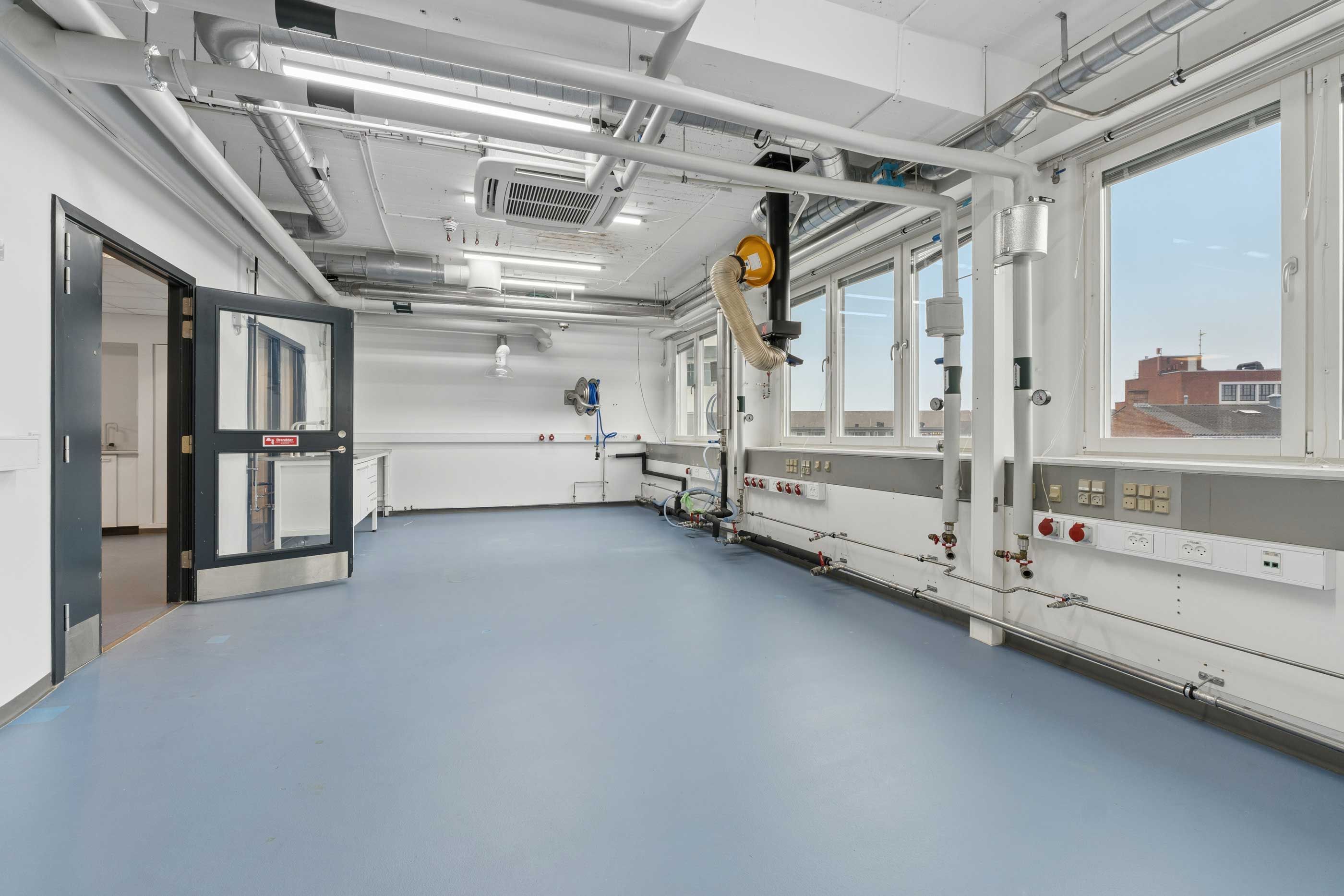 Laboratorium med moderne indretning og hvide vægge, høje vinduer, åbne glasdøre og lyse loftslampe.