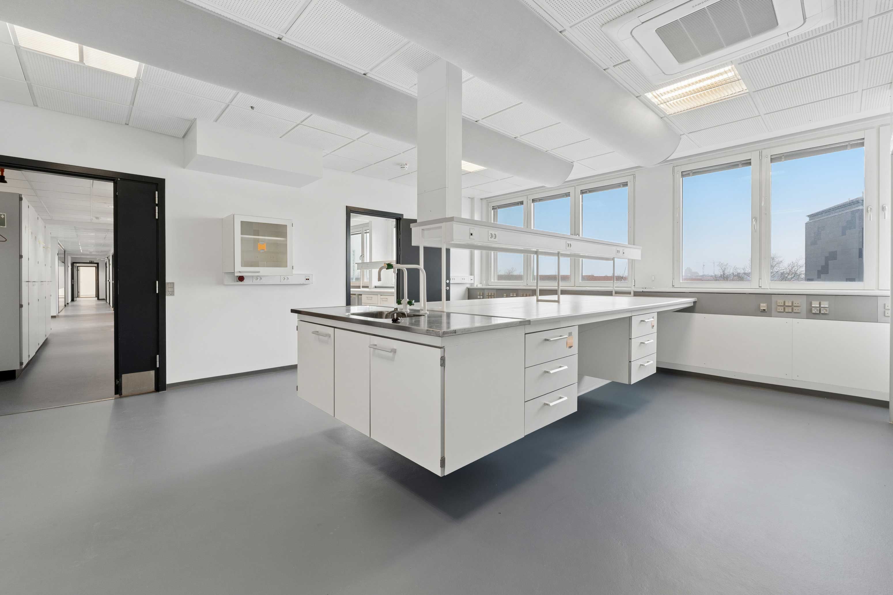 Lyst laboratorium med lyse lofter og højt til loftet, udstyret med flere højteknologiske apparater og lysevinduer, der sikrer godt lys og et åbent rum