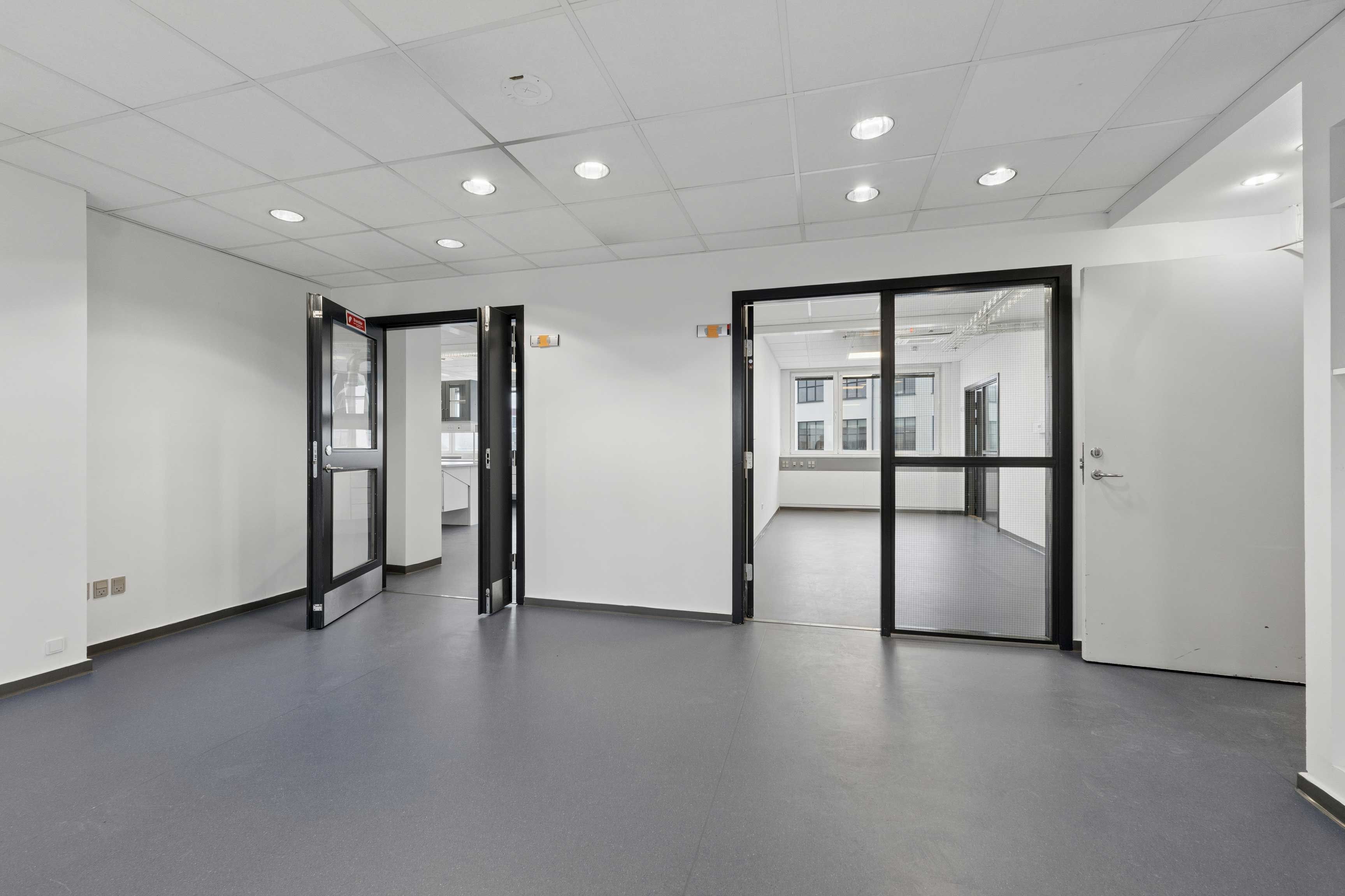 En lys, moderne laboratorie- og kontorbygning med glasdøre og hvide vægge. Det er en nyistandsat ejendom på Rønnegade 4 i København Ø.