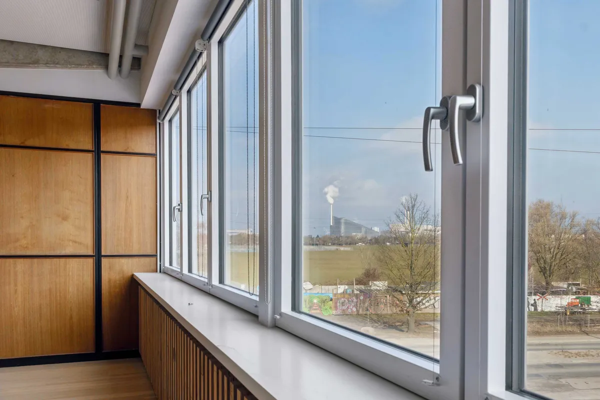 Vindueskarmen med udsigt til en stor bygning i baggrunden og skraldespand i forgrunden