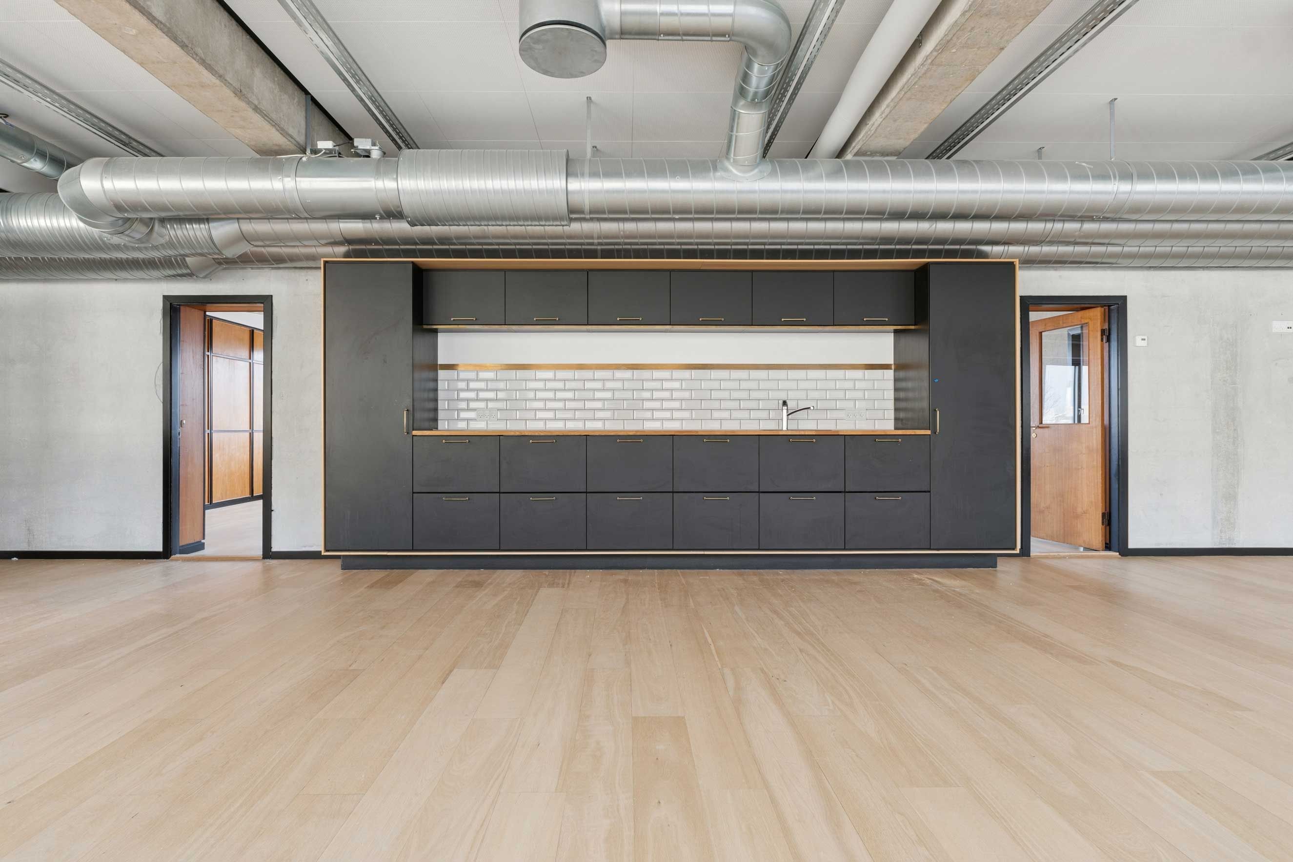 Indeni kontorlejemål med masser af muligheder til indretning. Moderne, lyse værelser med trægulv og industrielle loftsbjælker. Sorte, smukke skabe med håndtag og indbygget vandhane.