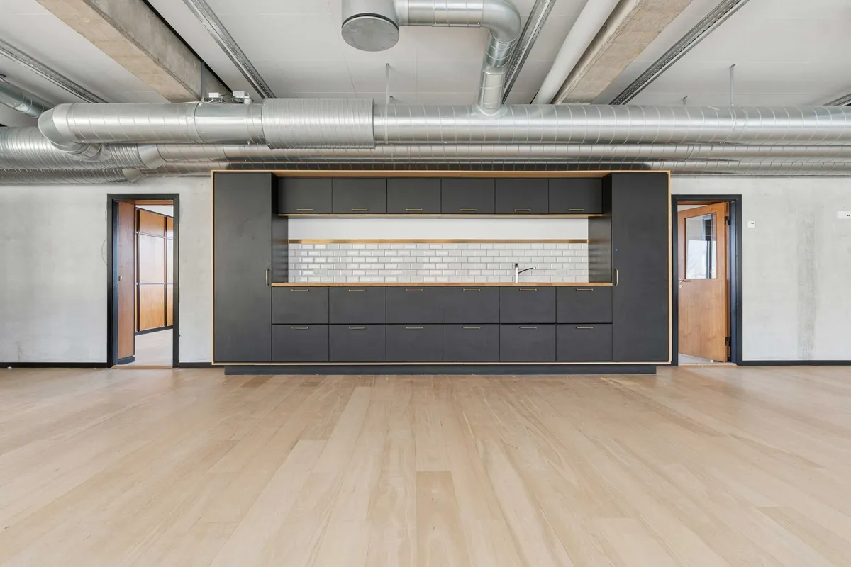 Indeni kontorlejemål med masser af muligheder til indretning. Moderne, lyse værelser med trægulv og industrielle loftsbjælker. Sorte, smukke skabe med håndtag og indbygget vandhane.