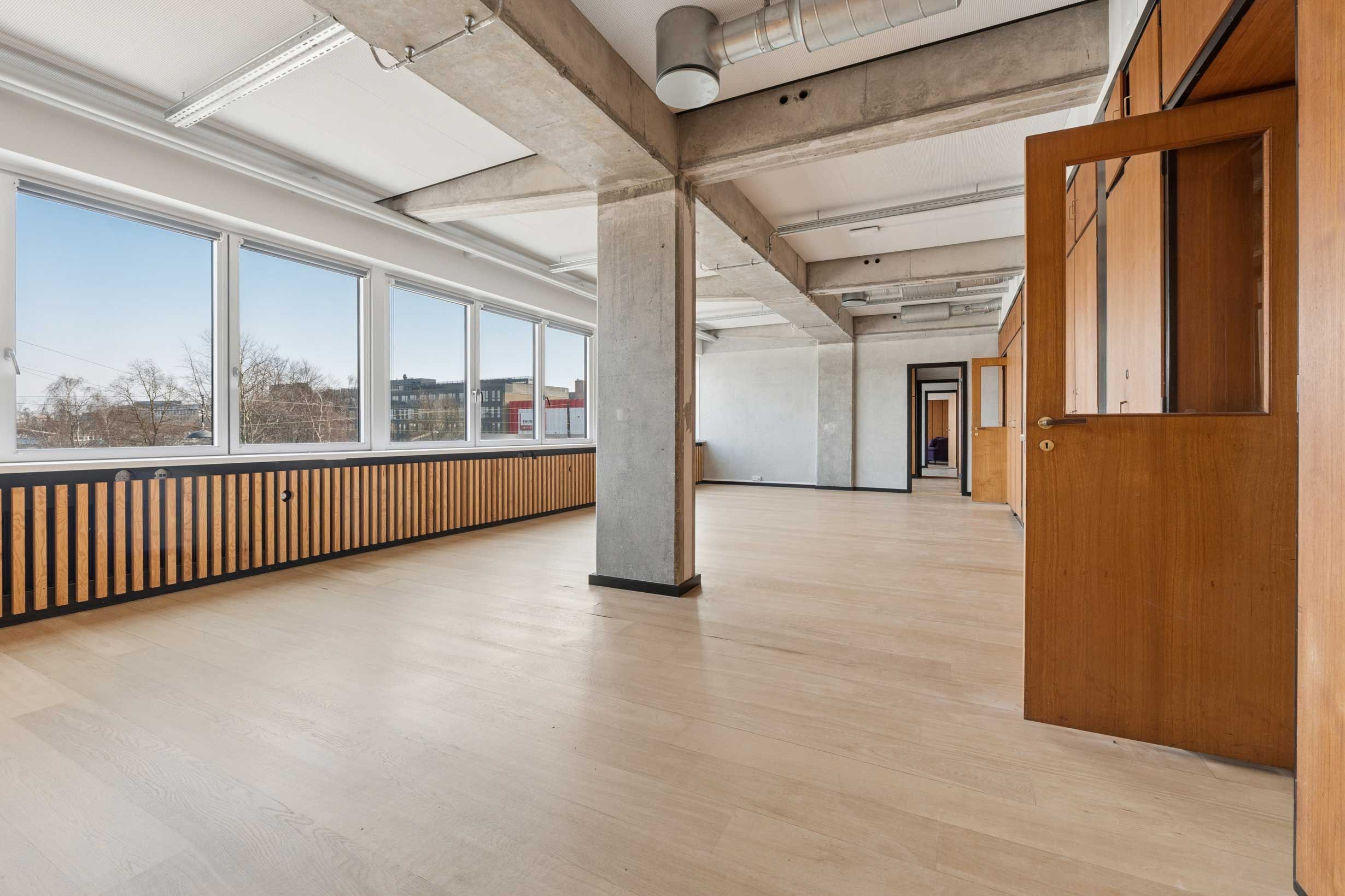 Moderne kontor med højloft og store vinduer, lyse rum og træpaneler, slank gulvbelægning og åbne døre til andre rum