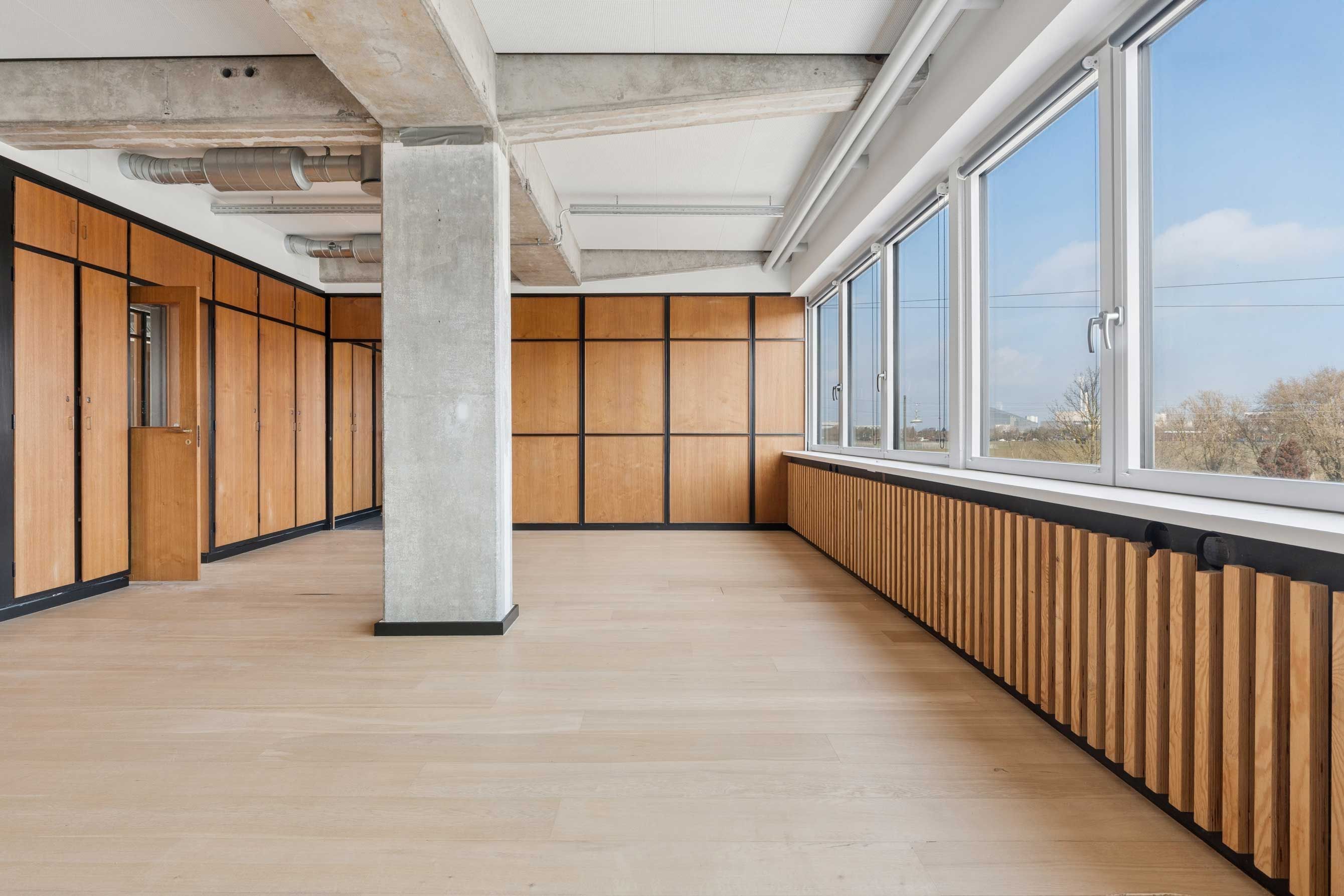 En stor åben lejlighed med træpaneler og gulvtæppe samt store vinduer med udsigt til byen