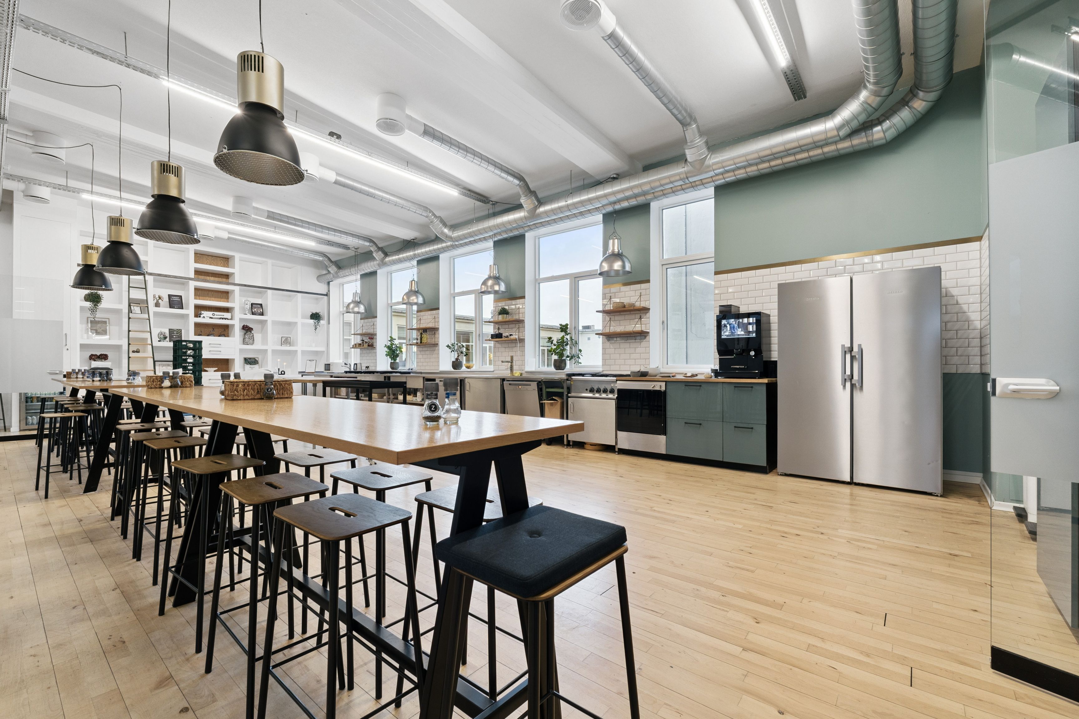 Kontorlokaler med åben køkkendel, lyse loftslamper og trægulv samt møbler og udstyr til rådighed i et industrielt miljø