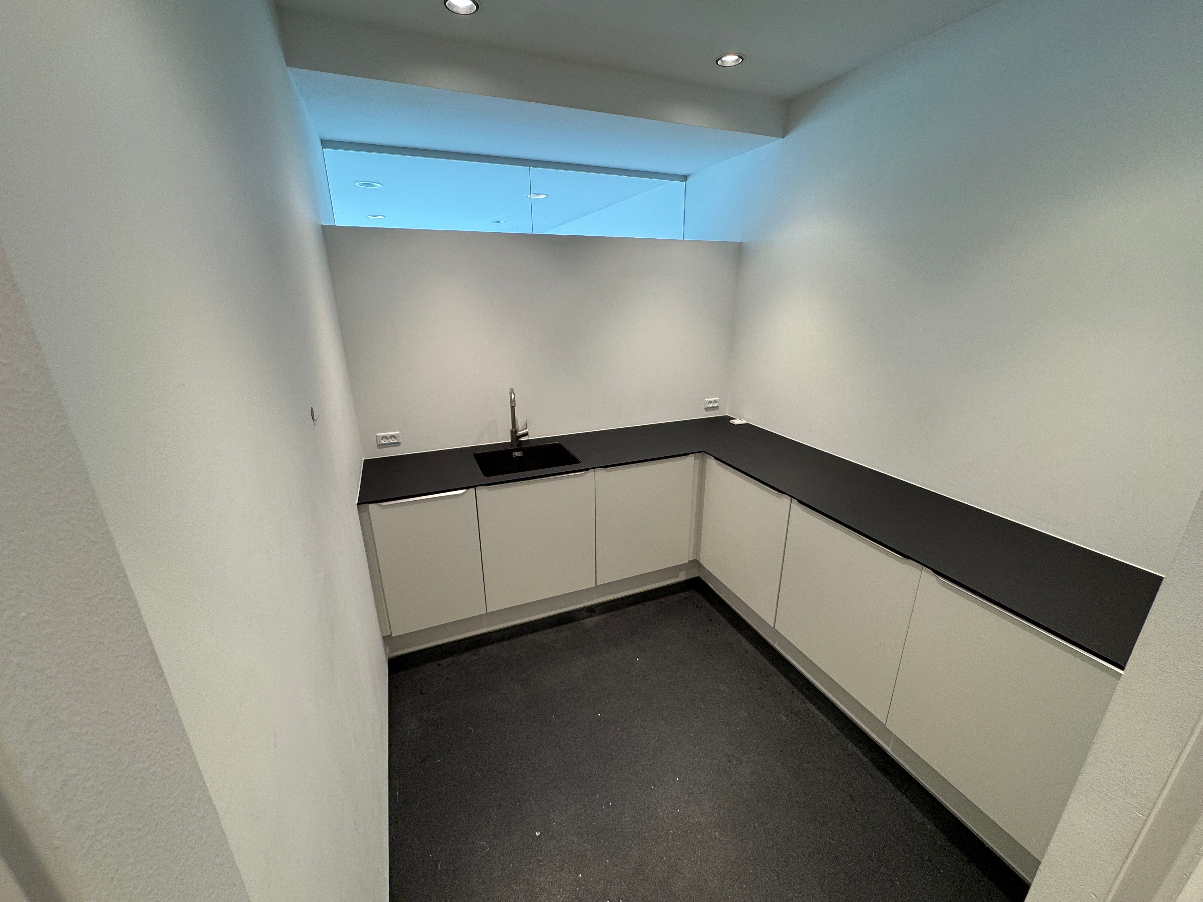 Showroom med hvidt loft, hvide vægge og sort bordplade, højt loft med vinduesglas og hvidt loft, svart gulv og en sort og hvid vask