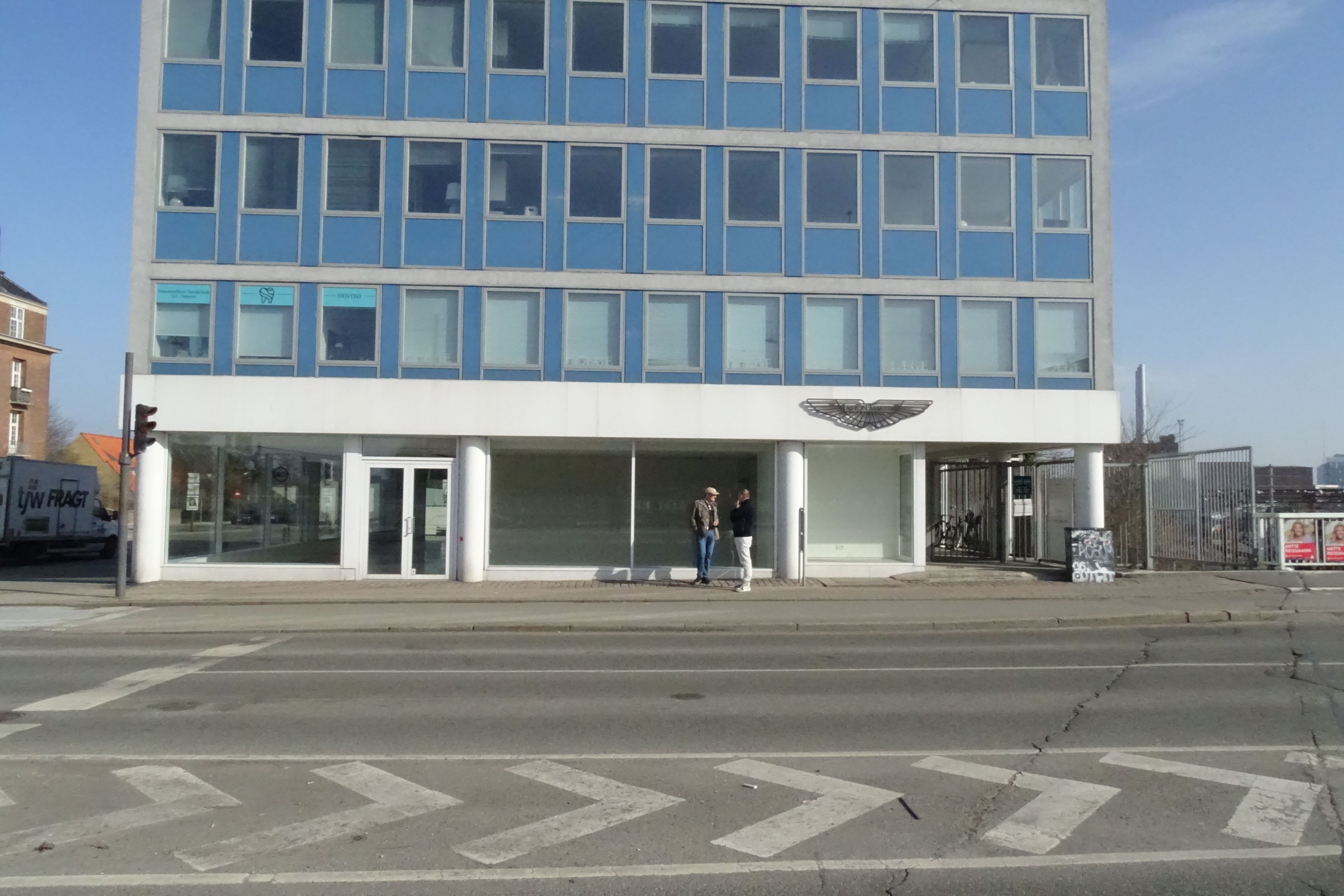 To mænd står foran et lukket showroom med en vægmaling af en ørn og teksten "dentist" i vinduet