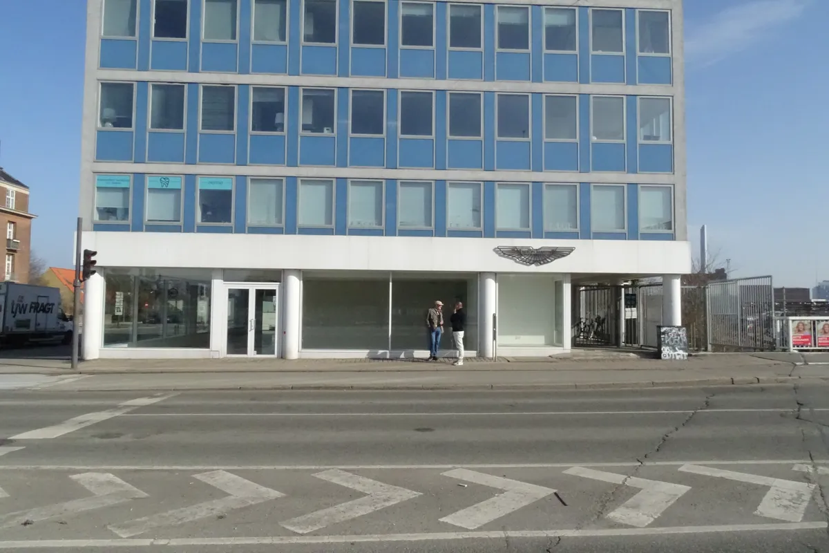 To mænd står foran et lukket showroom med en vægmaling af en ørn og teksten "dentist" i vinduet