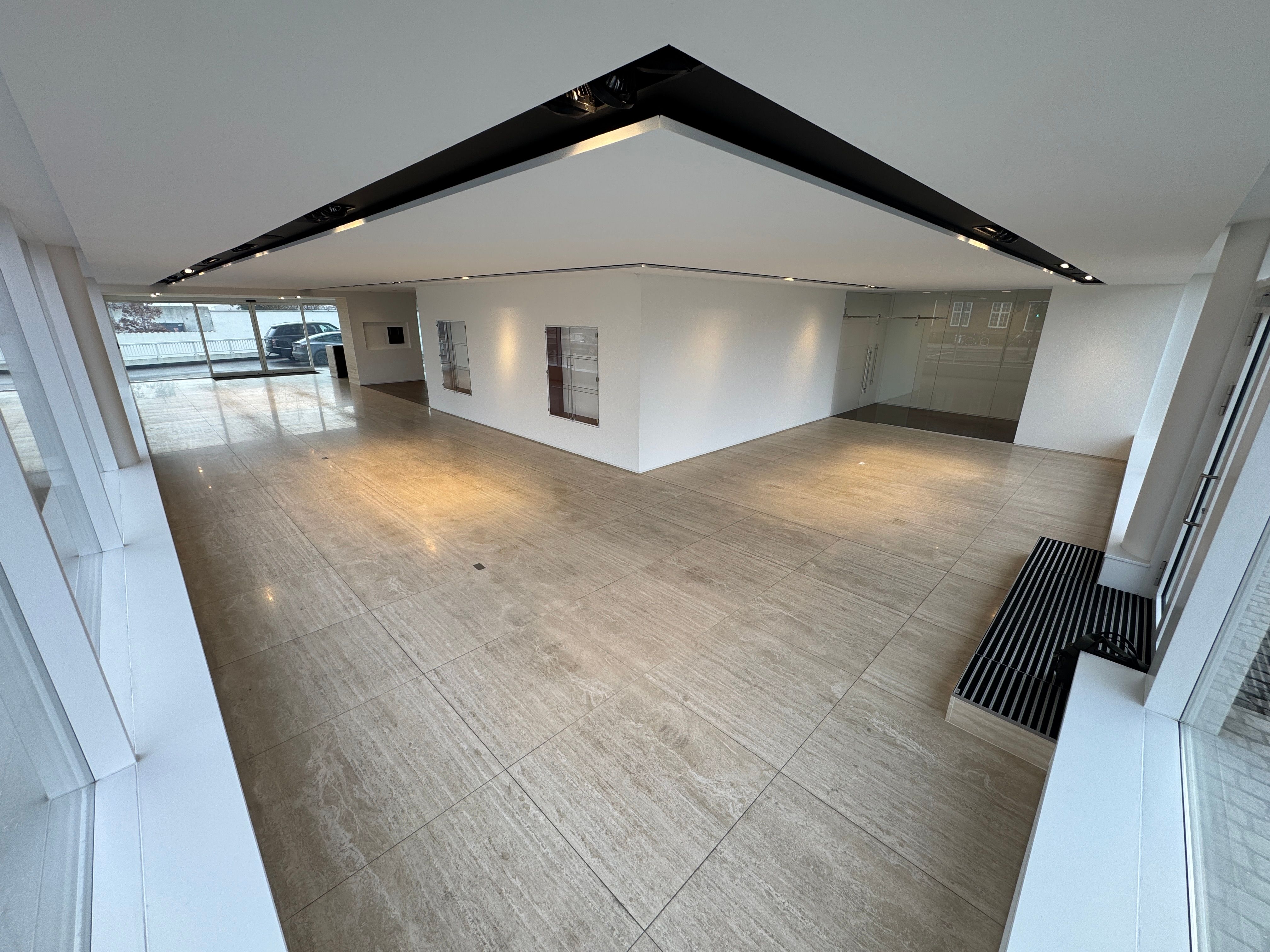 Moderne showroom med hvide vægge, gulv og loft, udstyret med glasvinduer og døre, samt en sort metalbænk og indbygget belysning