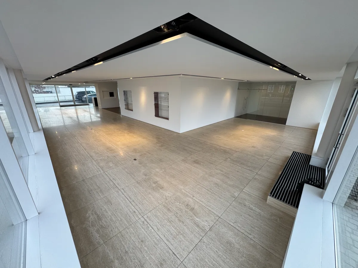 Moderne showroom med hvide vægge, gulv og loft, udstyret med glasvinduer og døre, samt en sort metalbænk og indbygget belysning