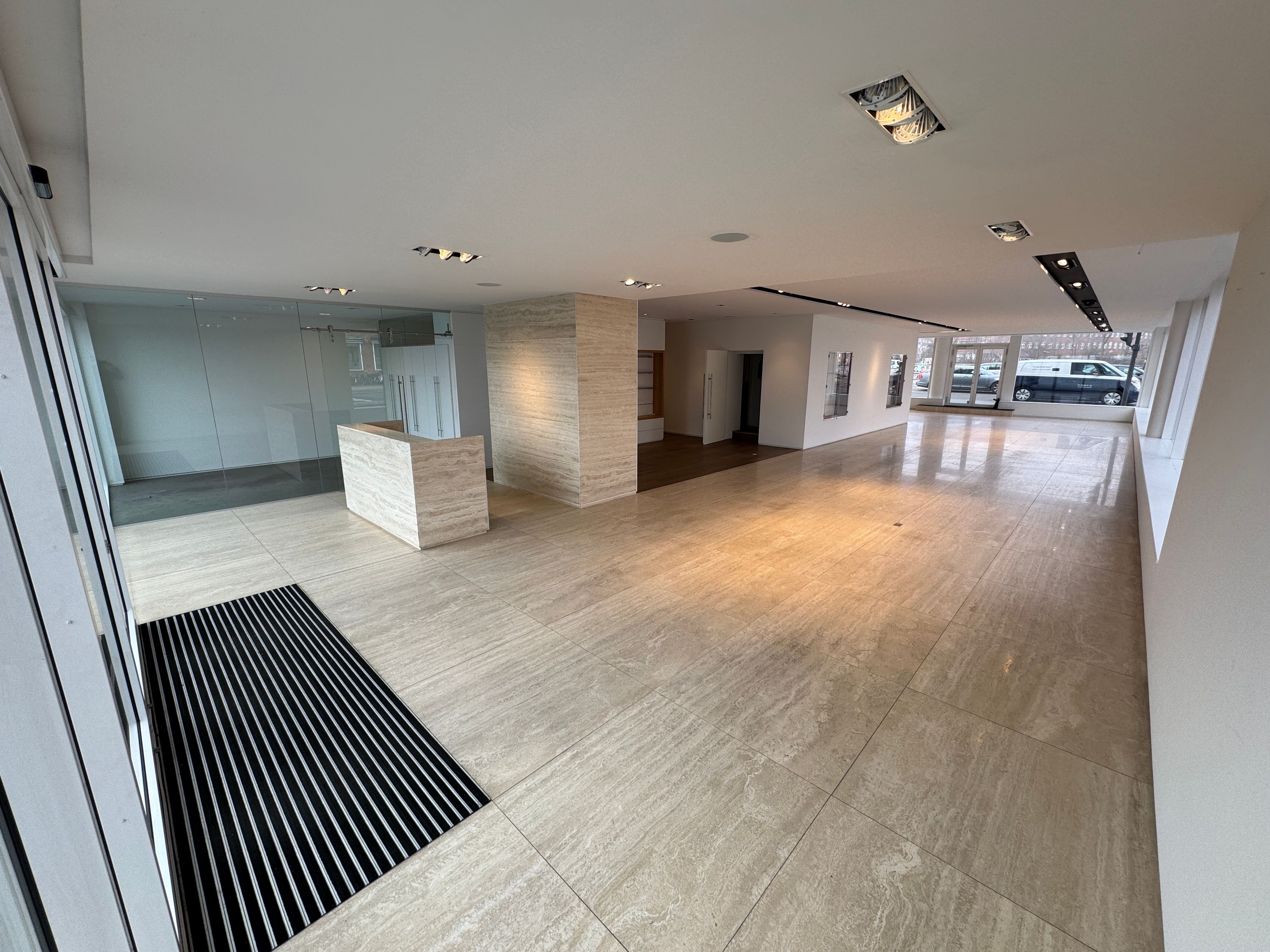 Elegant showroom med marmorgulve og glasdøre til leje i København. Minimalistisk design med højloft og moderne belysning. Solskin og biler udenfor.