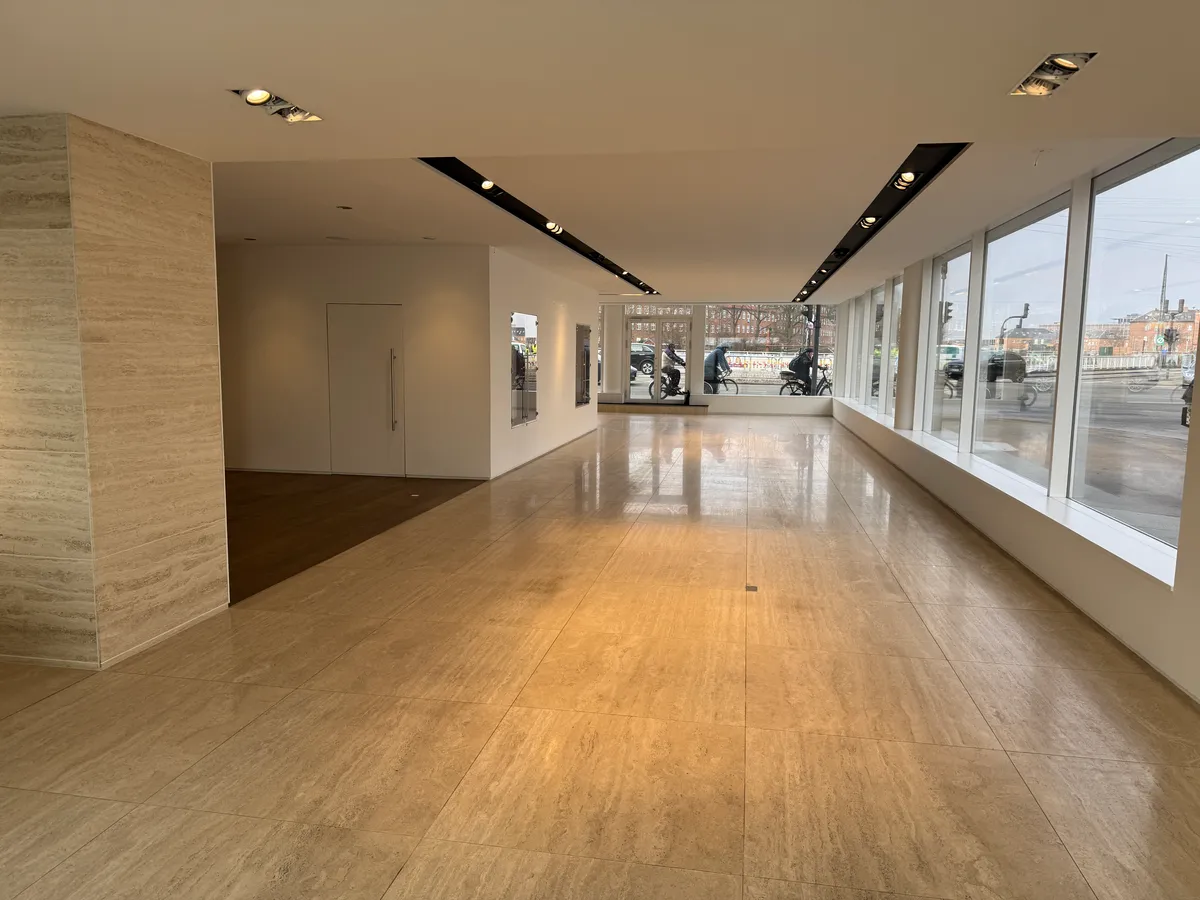 Et showroom med lyse gulvfliser og store vinduer med udsigt til gaden og cyklister