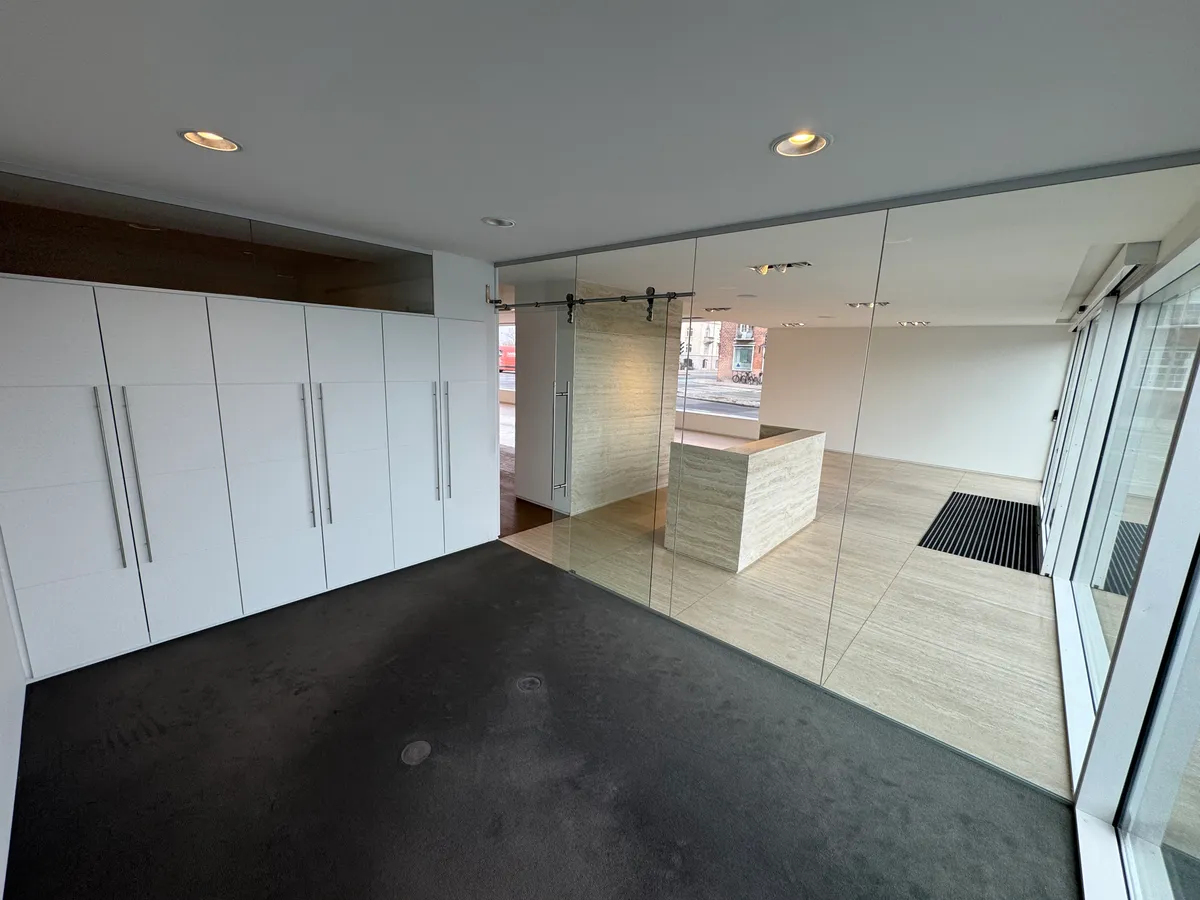 Store hvide garderobeskabe med håndtag og spejlede vægge med håndtag i gulv og loft. Der er gulvbelægning og spejle i loft og vægge.