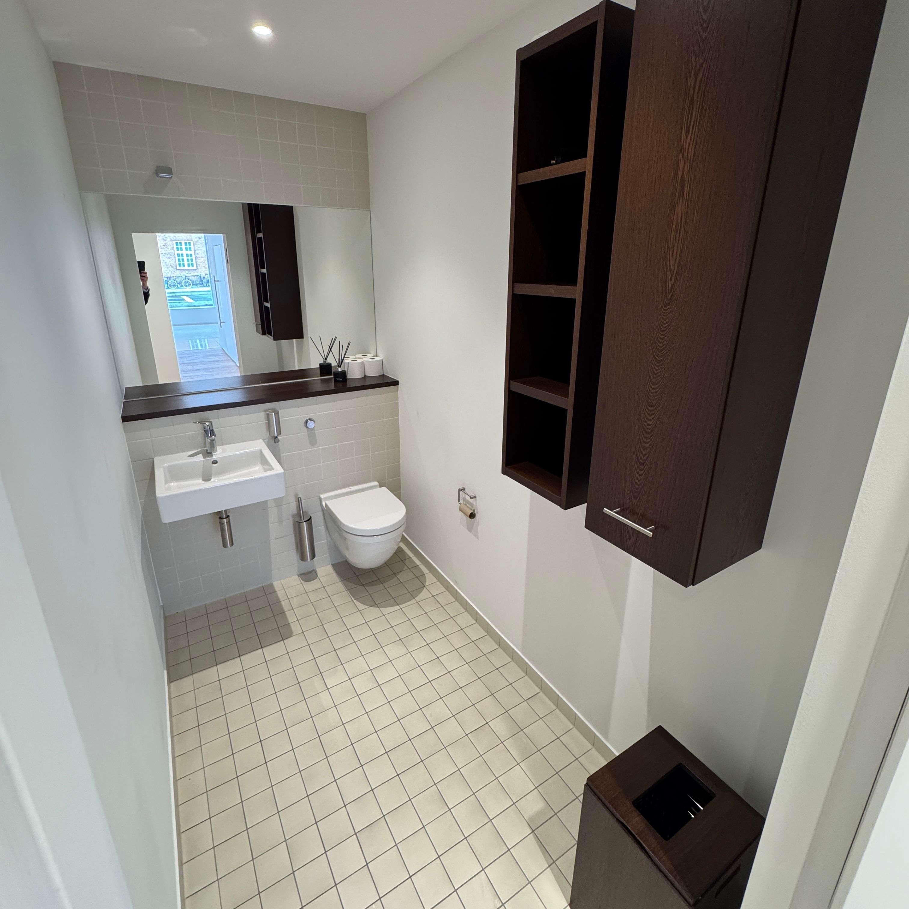 Toilet med hvidt toilet, hvidt vask og brusekabine samt lysegrå flisegulv og høj kvalitet møbler og indretning i lyse farver