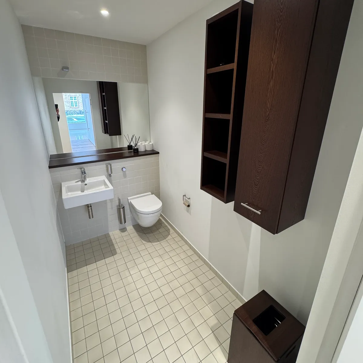 Toilet med hvidt toilet, hvidt vask og brusekabine samt lysegrå flisegulv og høj kvalitet møbler og indretning i lyse farver