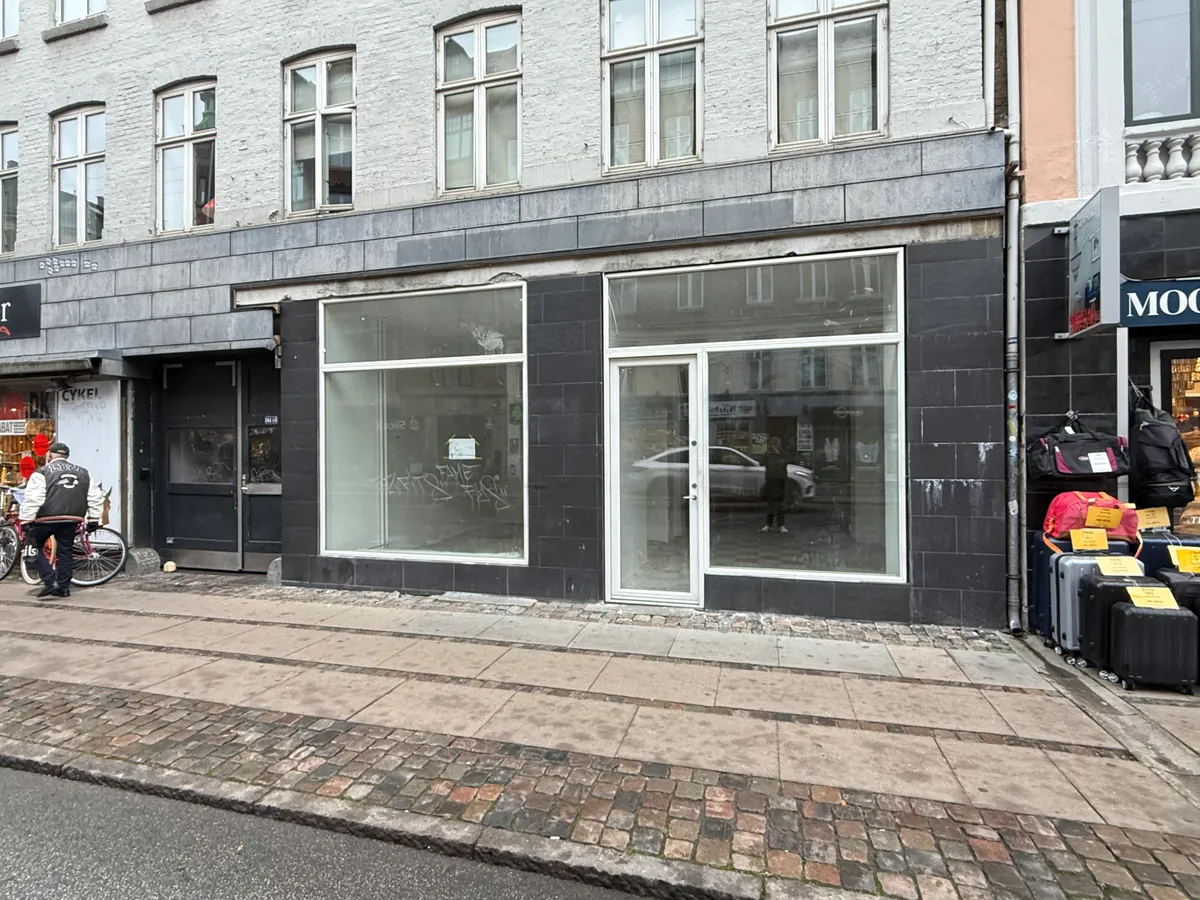 En mand står med sin cykel ved en glasdør på Nørrebrogade, og der er flere rejsekuffert og rygsække udstillet foran en butik