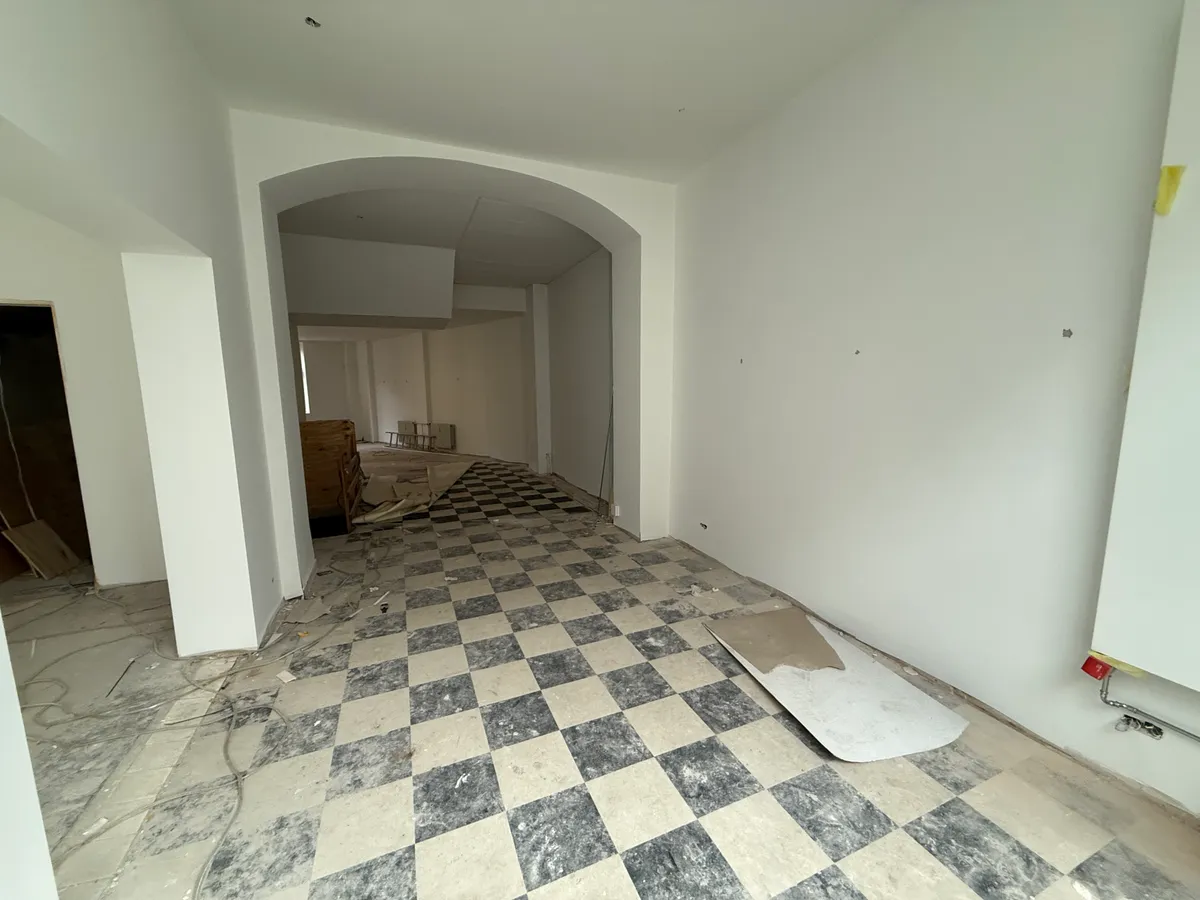 En tom restaurant med trægulve og hvide vægge på Nørrebrogade. Der er en bjælke over gulvet og kabelstrimler på gulvet. Der er også et stykke papir på gulvet.