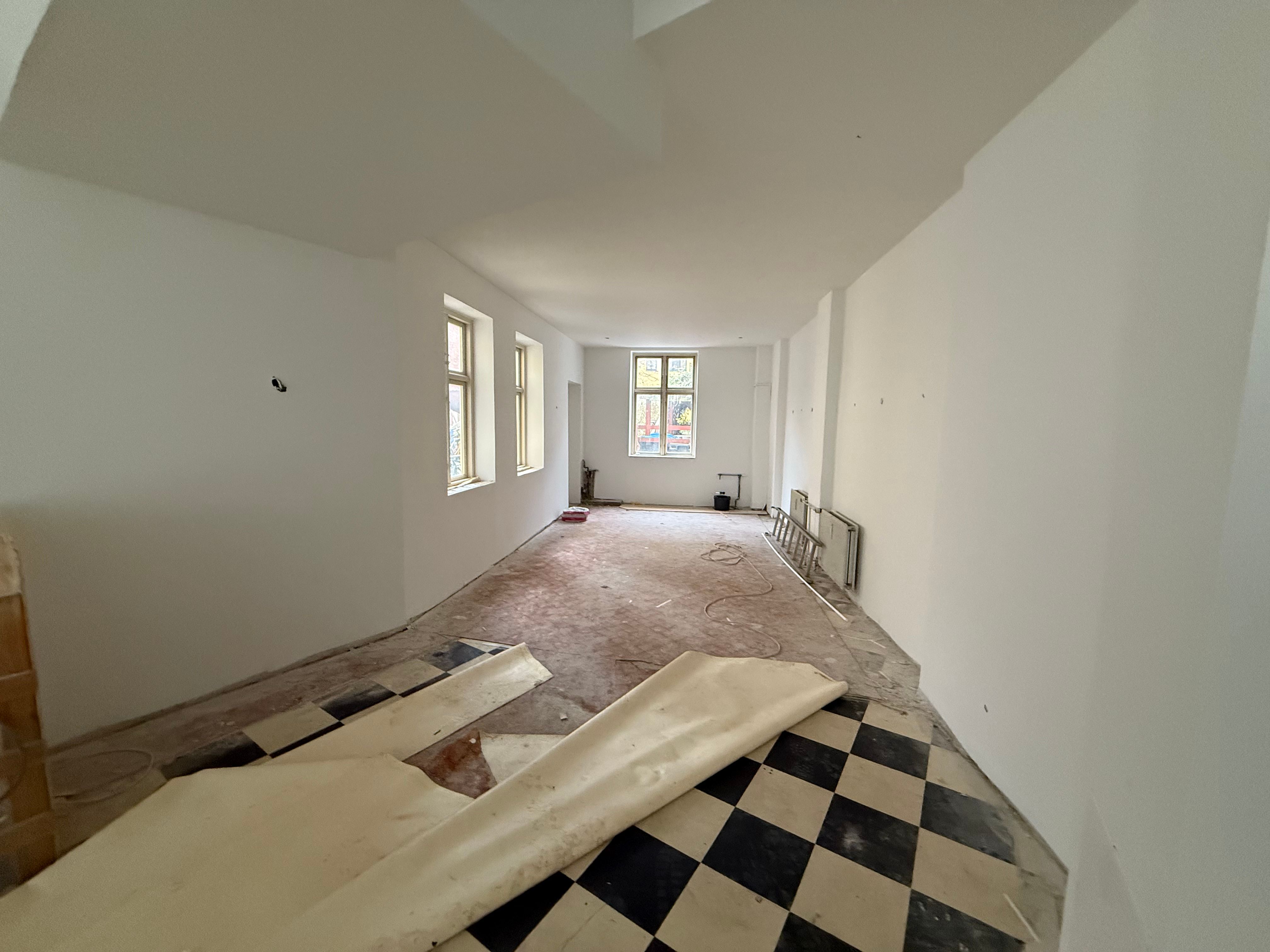 En tom restaurant med et sort og hvidt krydsmønster på gulvet og store vinduer langs væggen