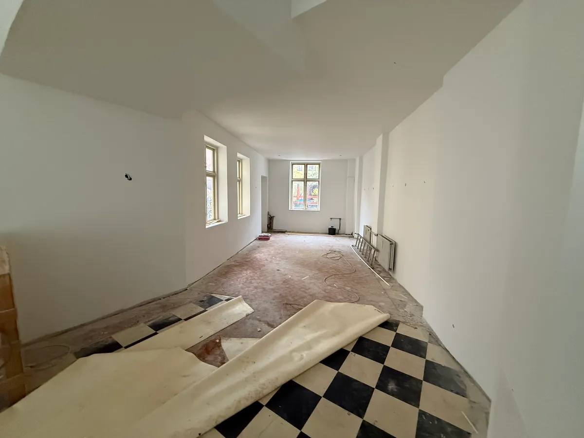 En tom restaurant med et sort og hvidt krydsmønster på gulvet og store vinduer langs væggen