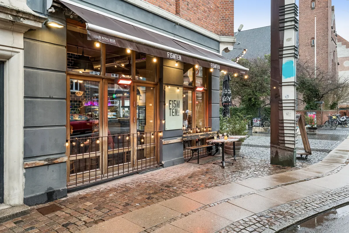 Restaurant med navnet Fisken Ten og udendørs spisning på Holmbladsgade i København S. Et bord og en køkkenhave med planter og en paraply. En bil og mennesker er synlige i vinduet