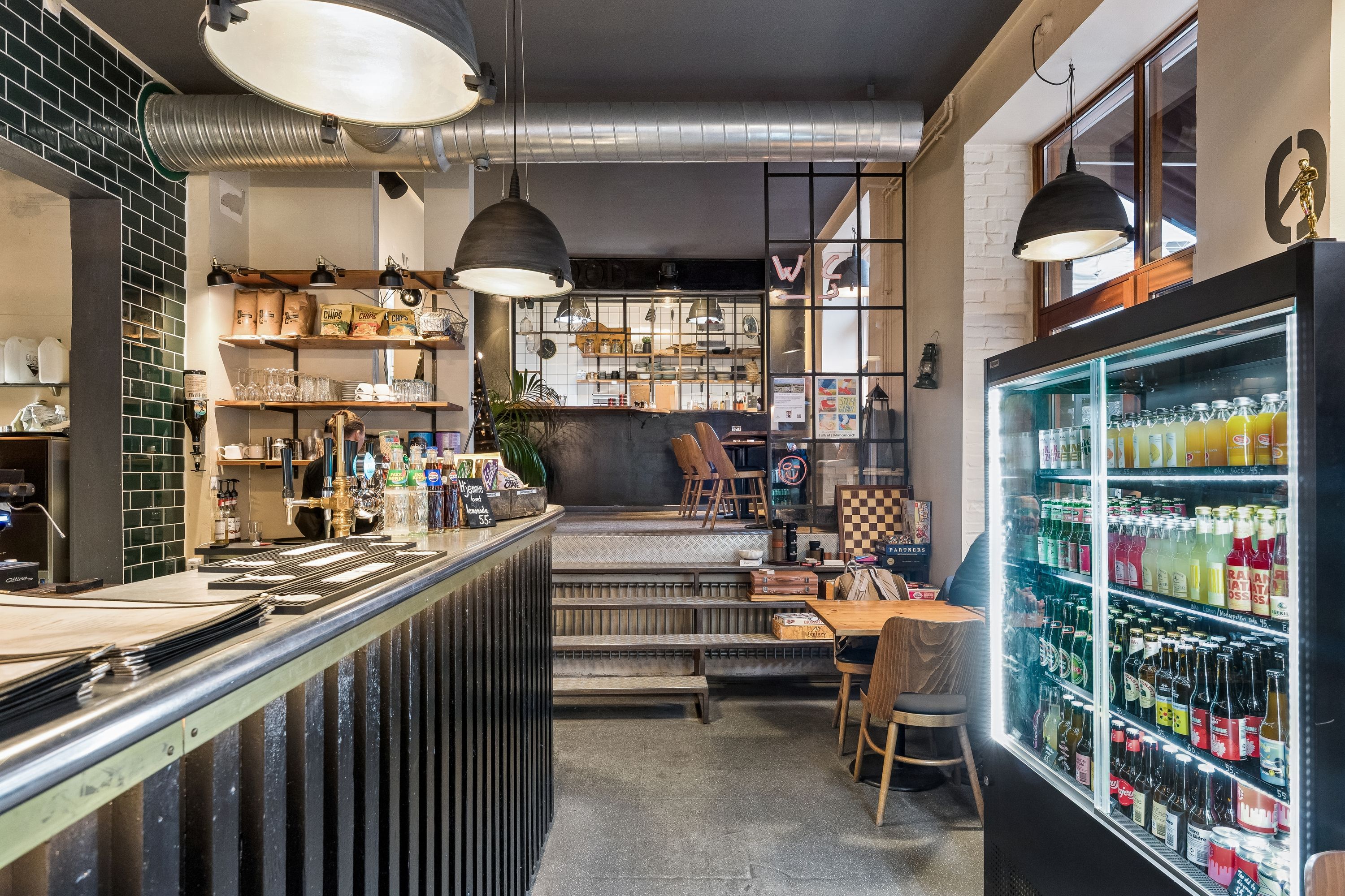 Restaurant med moderne interiør, gulv, møbler og briller, og et køleskab med drikkevarer på Holmbladsgade.