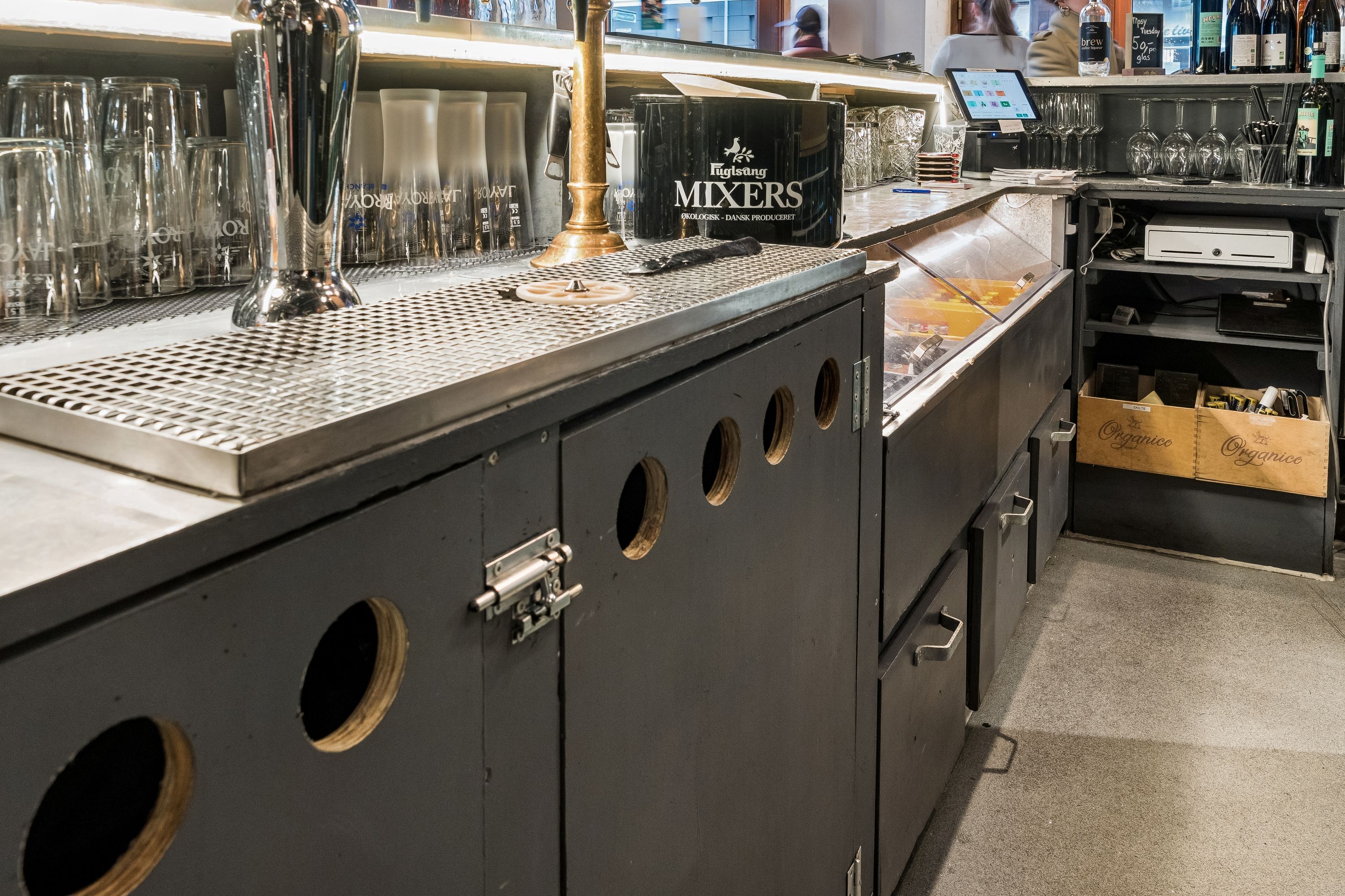 Restaurant med rustfri bar, glas, ølfat, mixers og vinflasker. Bar med skåle, tablet og øltønder samt køleskab med varer.